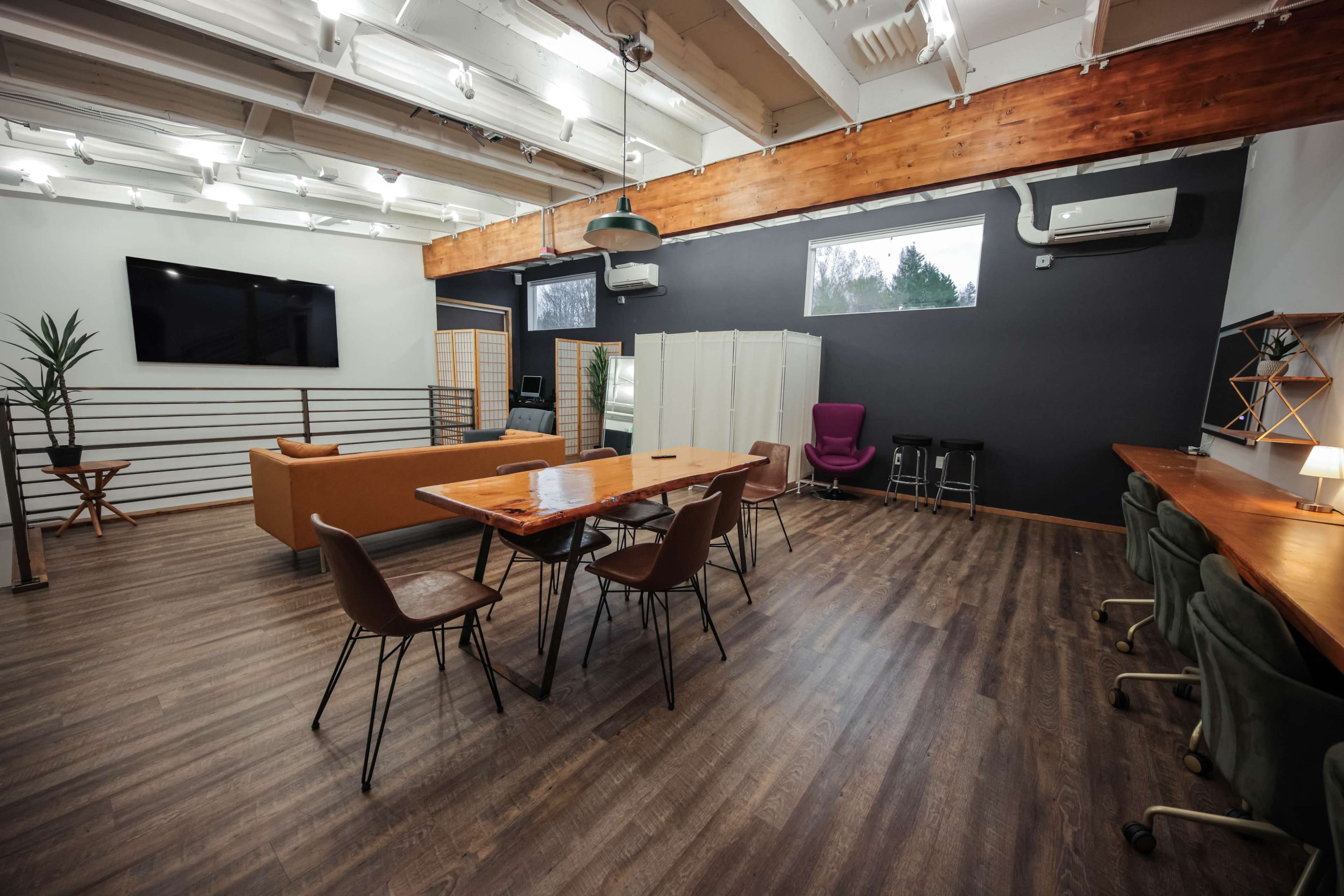 A modern co-working space with wooden beams, a large table surrounded by chairs, and various seating areas.