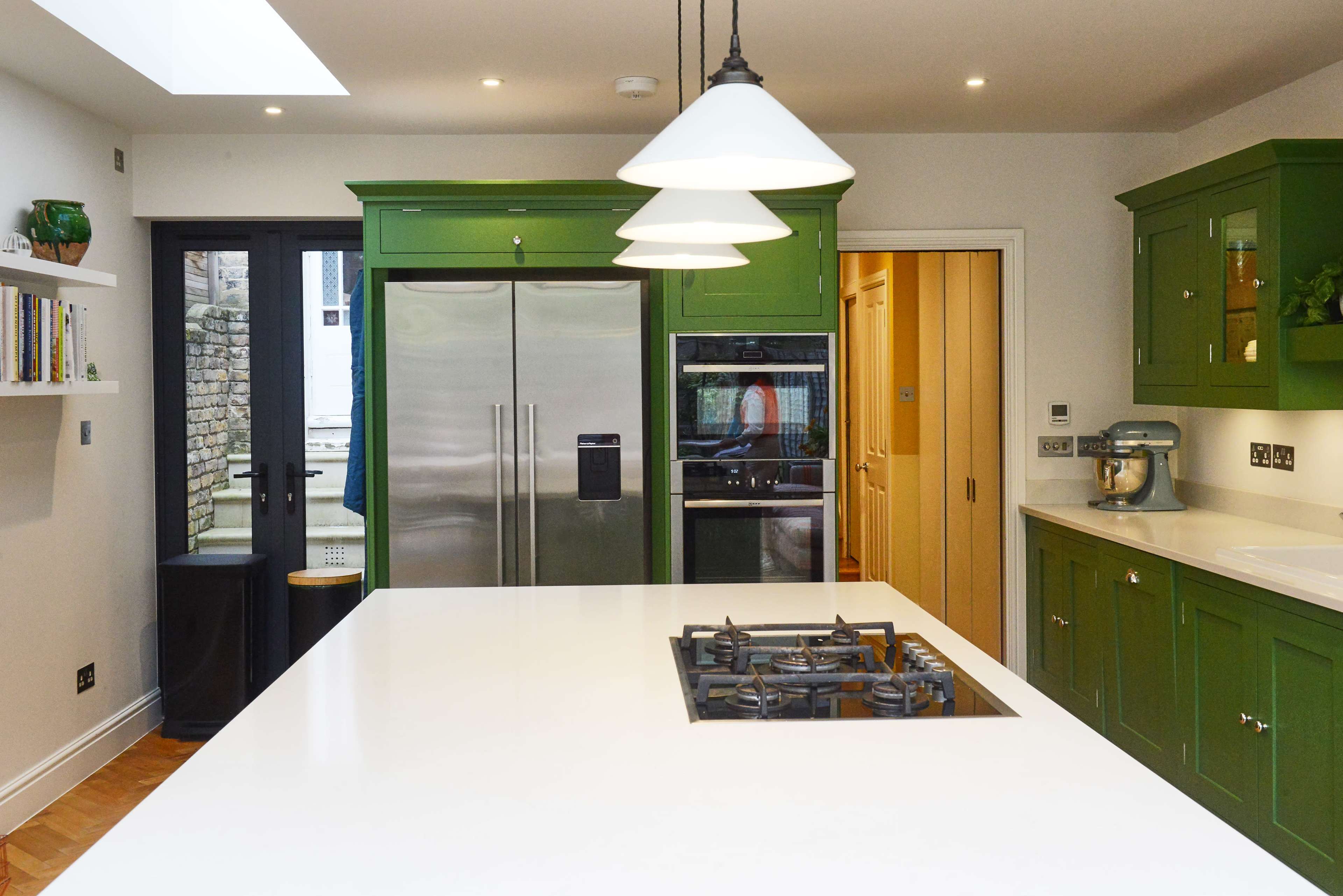 The kitchen features a large white island with a gas cooktop and green cabinetry, including a stainless steel refrigerator and an oven.