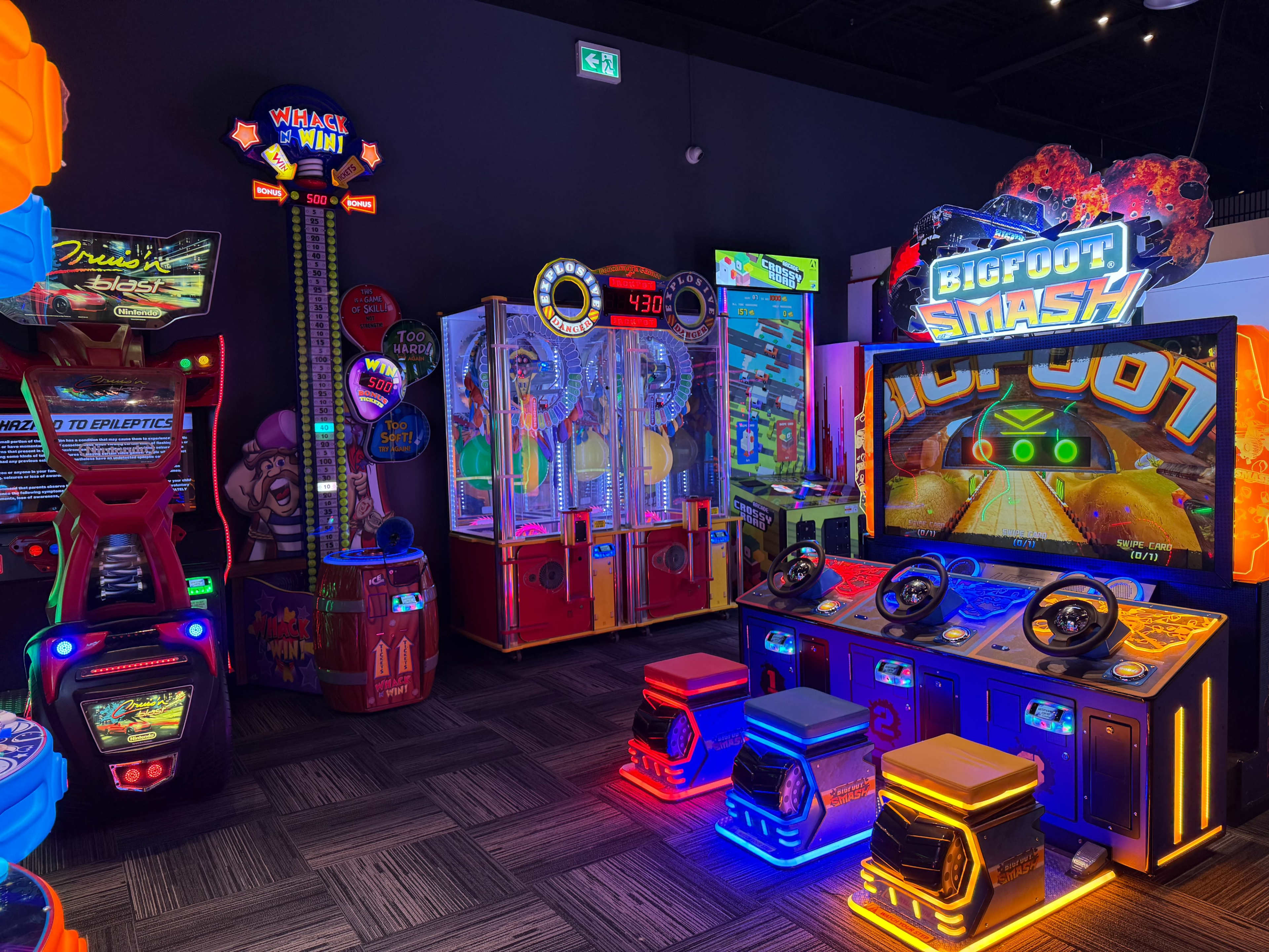 The image shows a vibrant arcade featuring various colorful games, including claw machines, racing games, and skill-based attractions, all illuminated by neon lights.