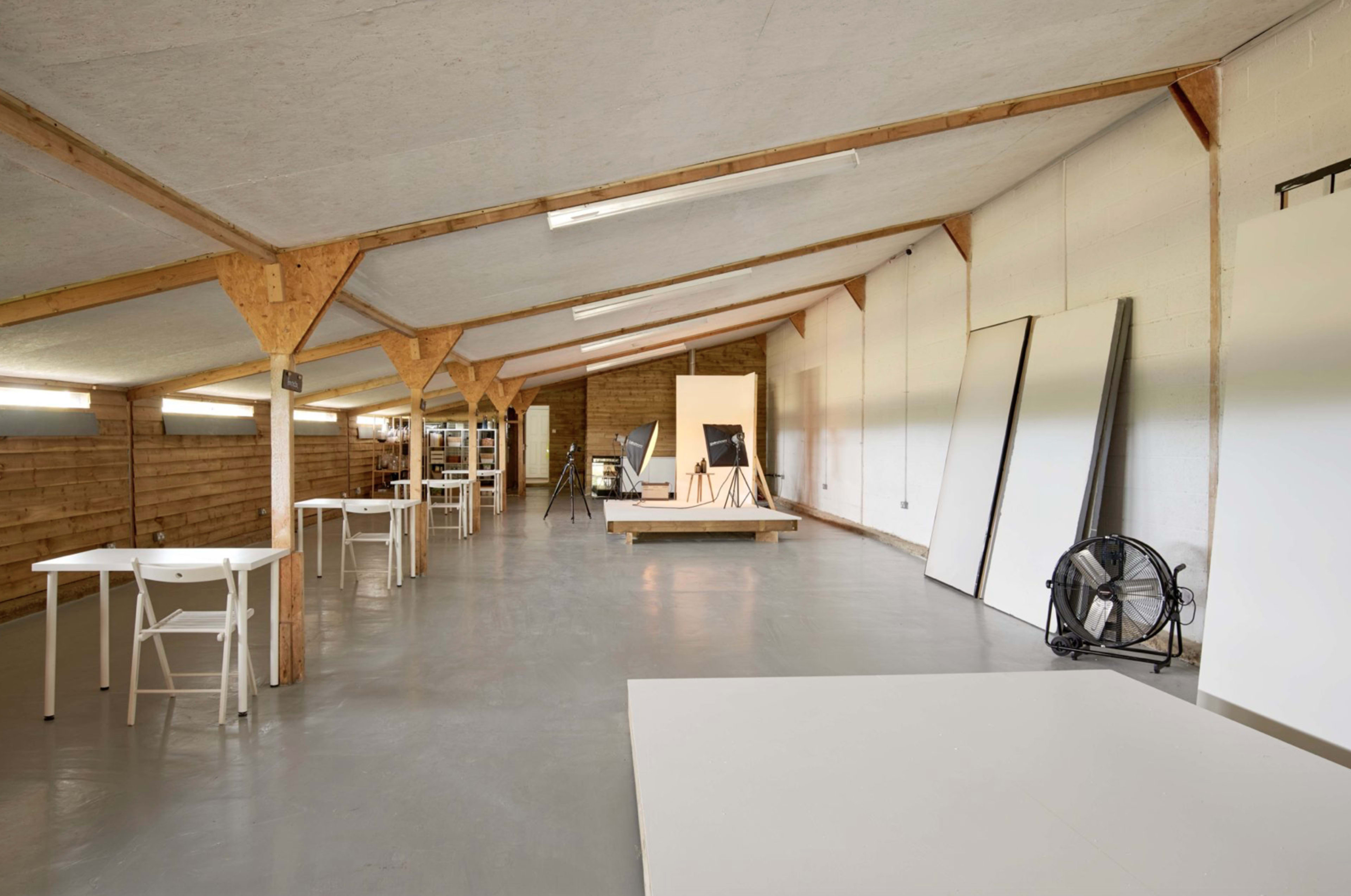 A spacious, well-lit artist studio with wooden beams, several tables, and large blank canvases leaning against the walls.