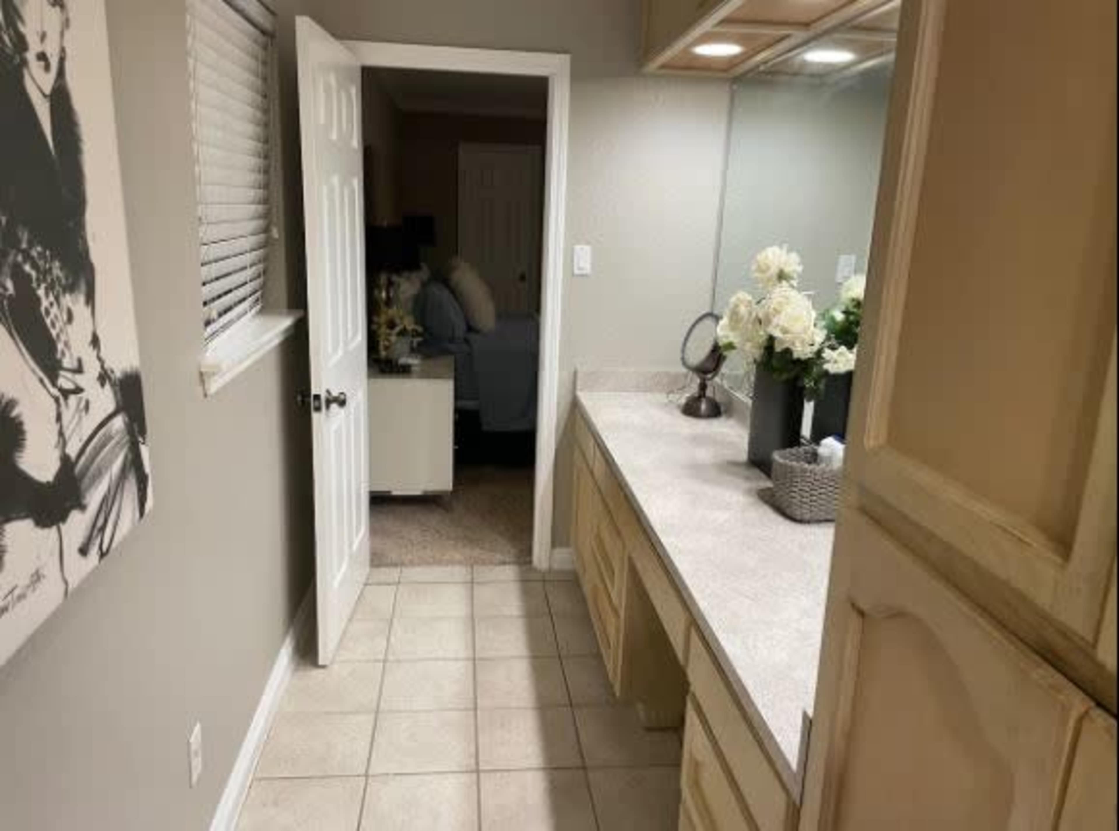 A hallway leading to a bedroom, with a vanity area featuring a countertop and a mirror, and a bouquet of flowers on display.