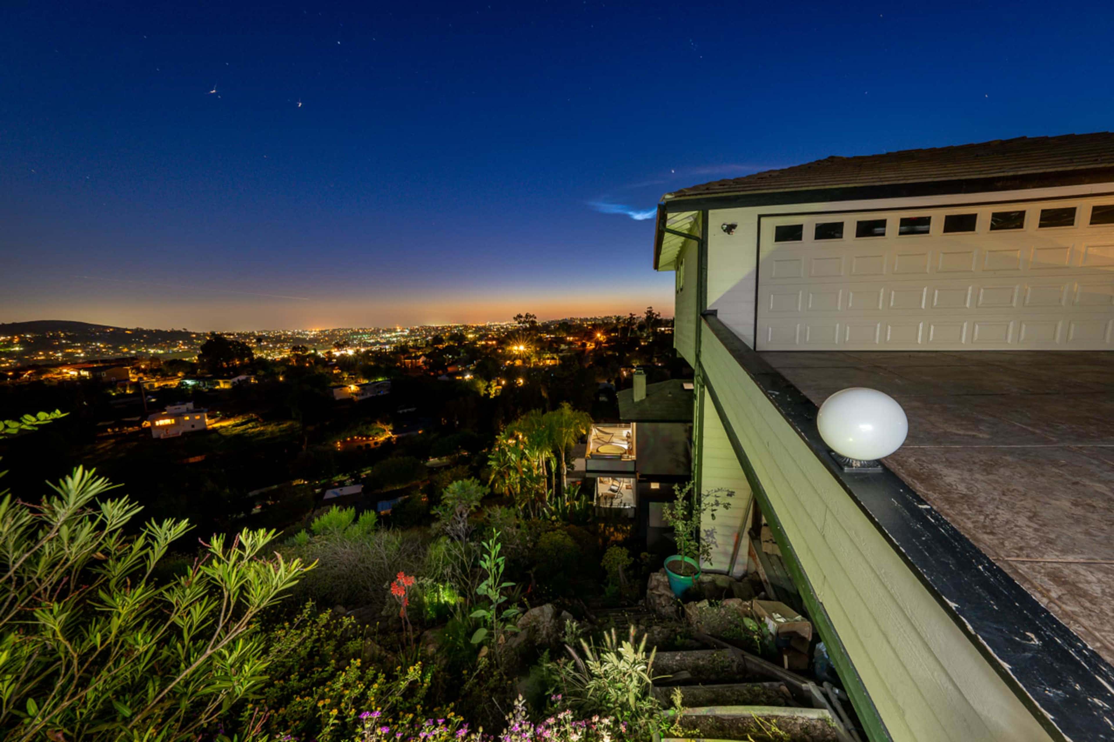 A hillside home overlooks a sprawling cityscape illuminated by city lights at dusk.