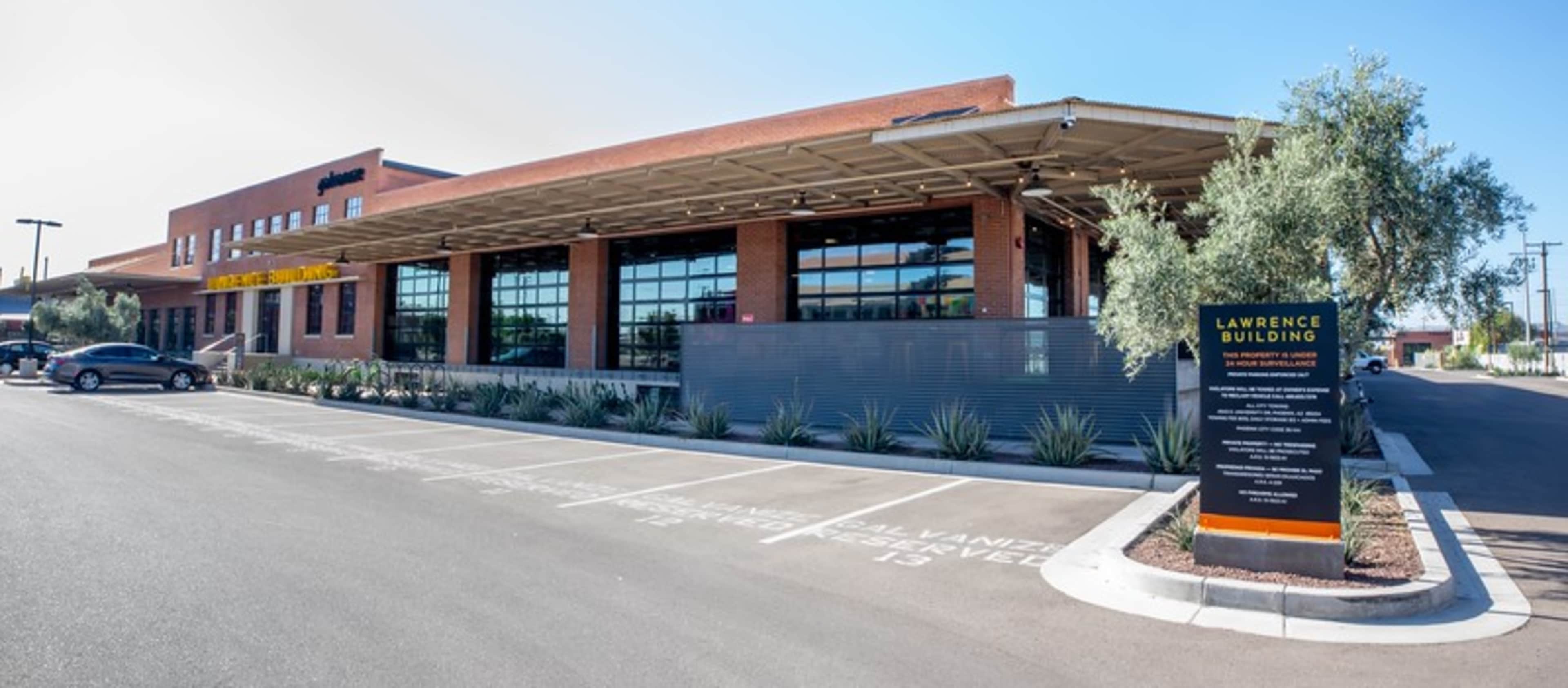 A modern brick building with large windows, a covered entrance, and a landscaped parking area labeled "Lawrence Building."