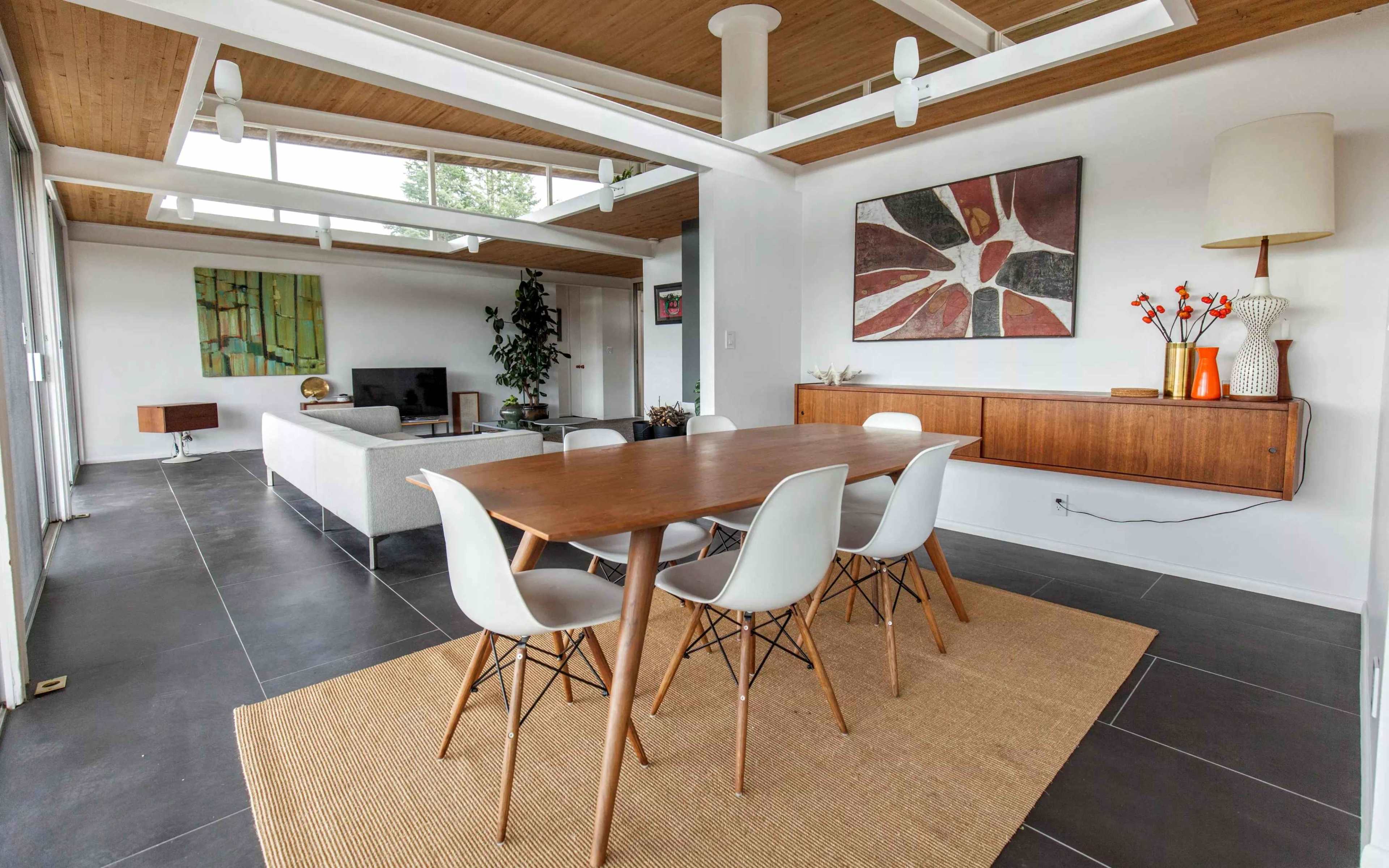A modern dining area featuring a wooden table surrounded by white chairs, with large windows and natural light illuminating the space.