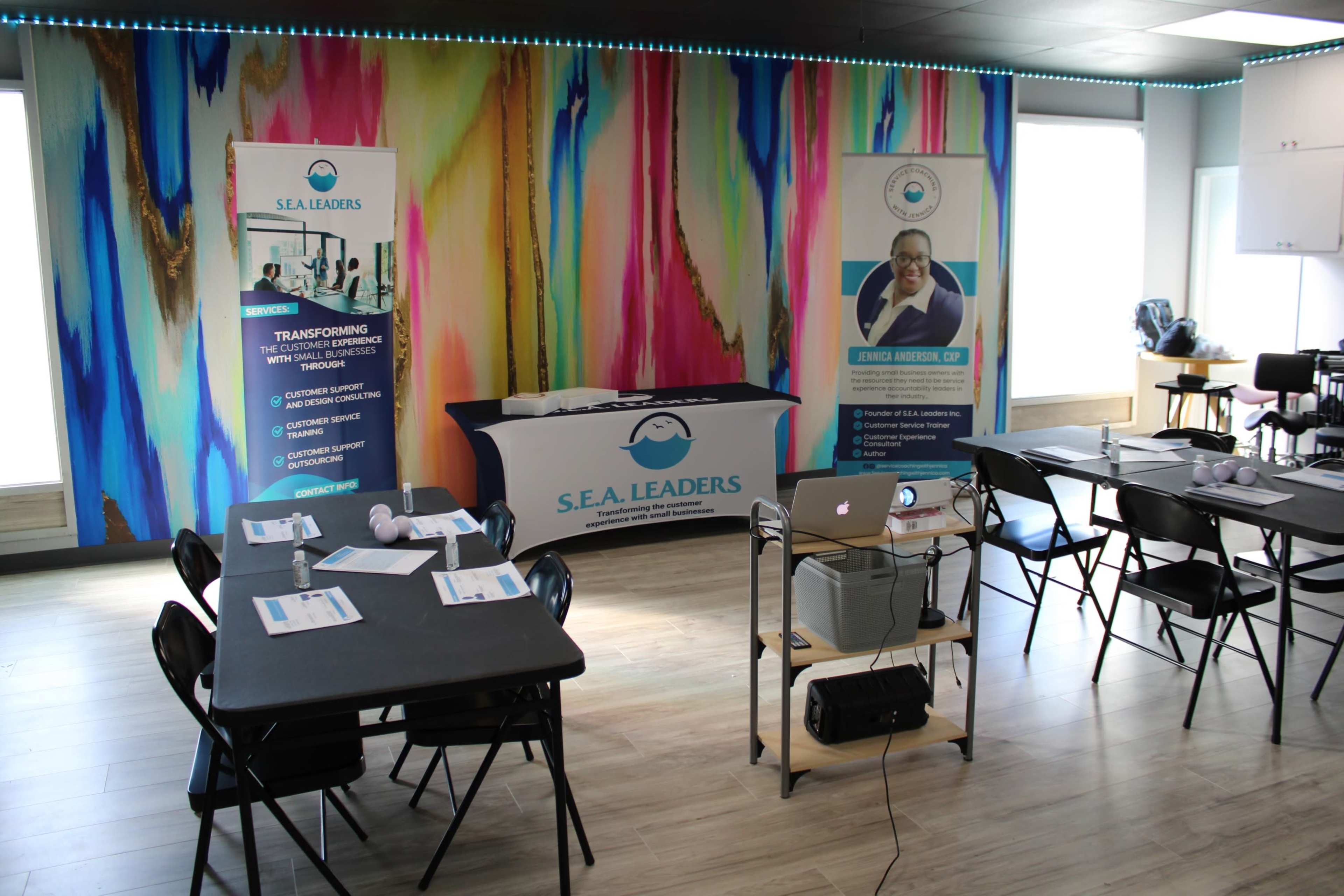 A training room setup with tables, chairs, promotional banners, and a projector against a colorful mural.