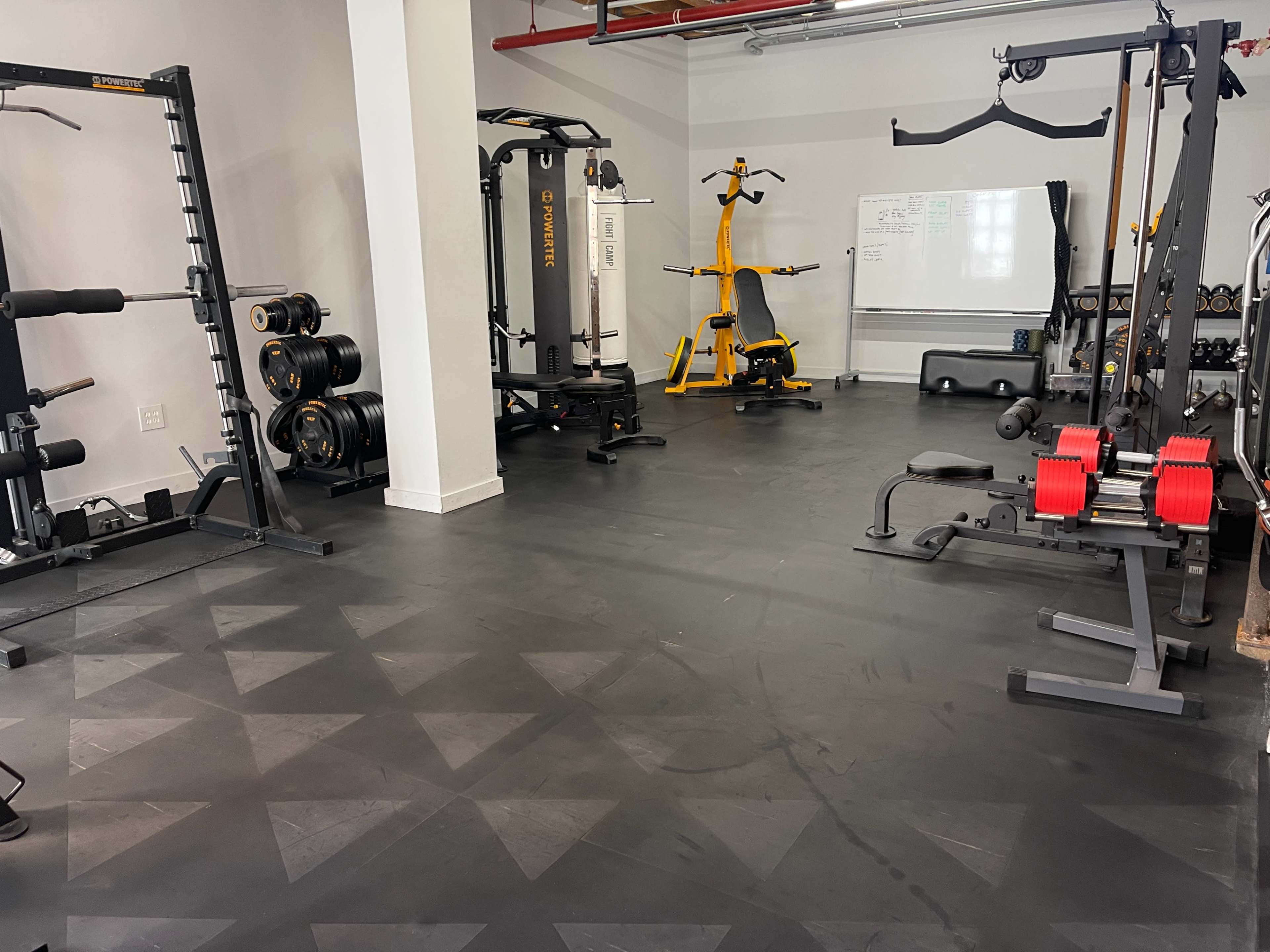 An organized gym interior with various exercise equipment, including weight machines, free weights, and a stationary bike, on a black floor.