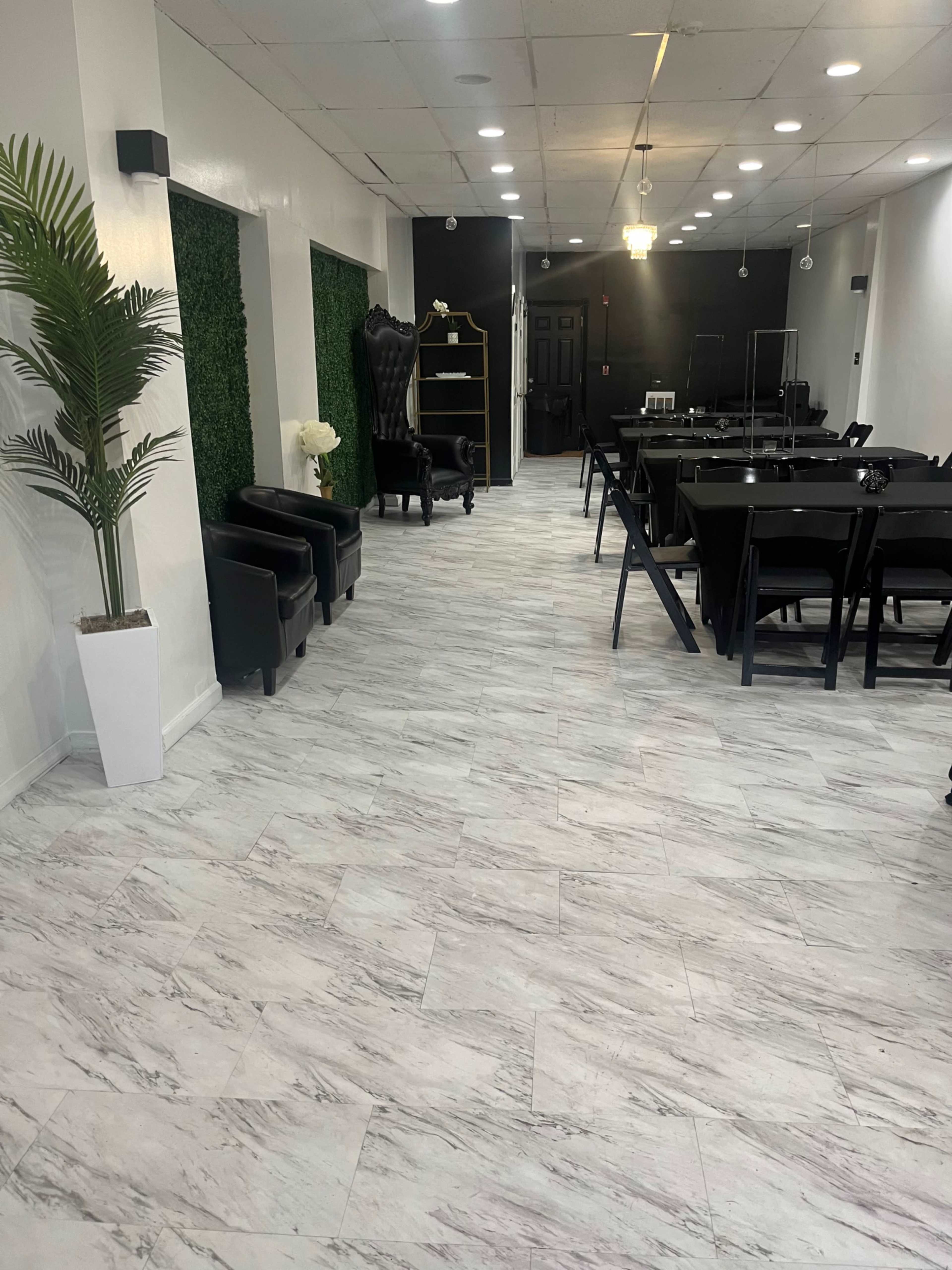 A modern interior space with a marble-patterned floor, black chairs, green accent walls, and a dining area arranged with tables.