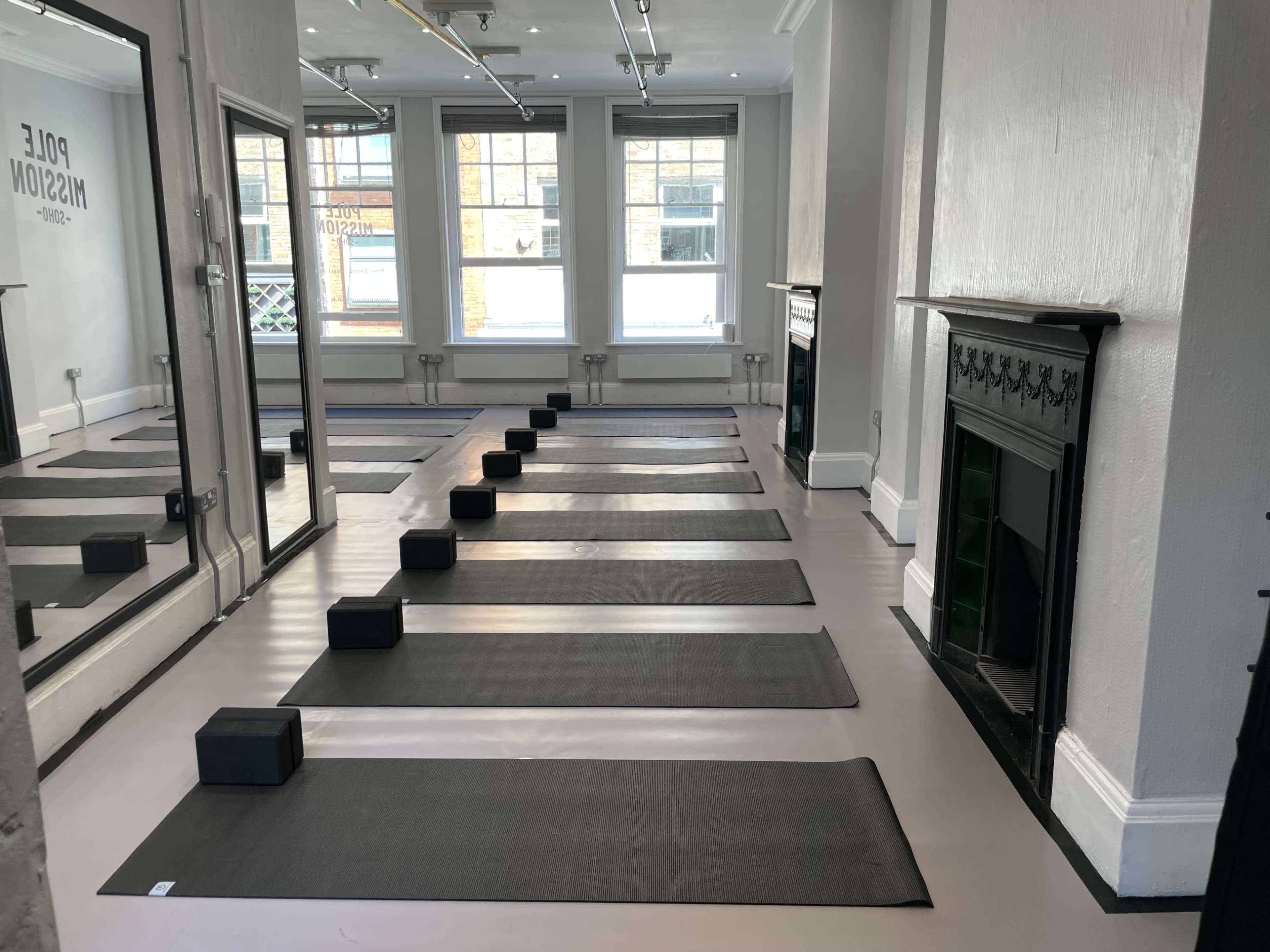 A spacious studio with several yoga mats arranged in rows and black blocks positioned at the front of each mat.