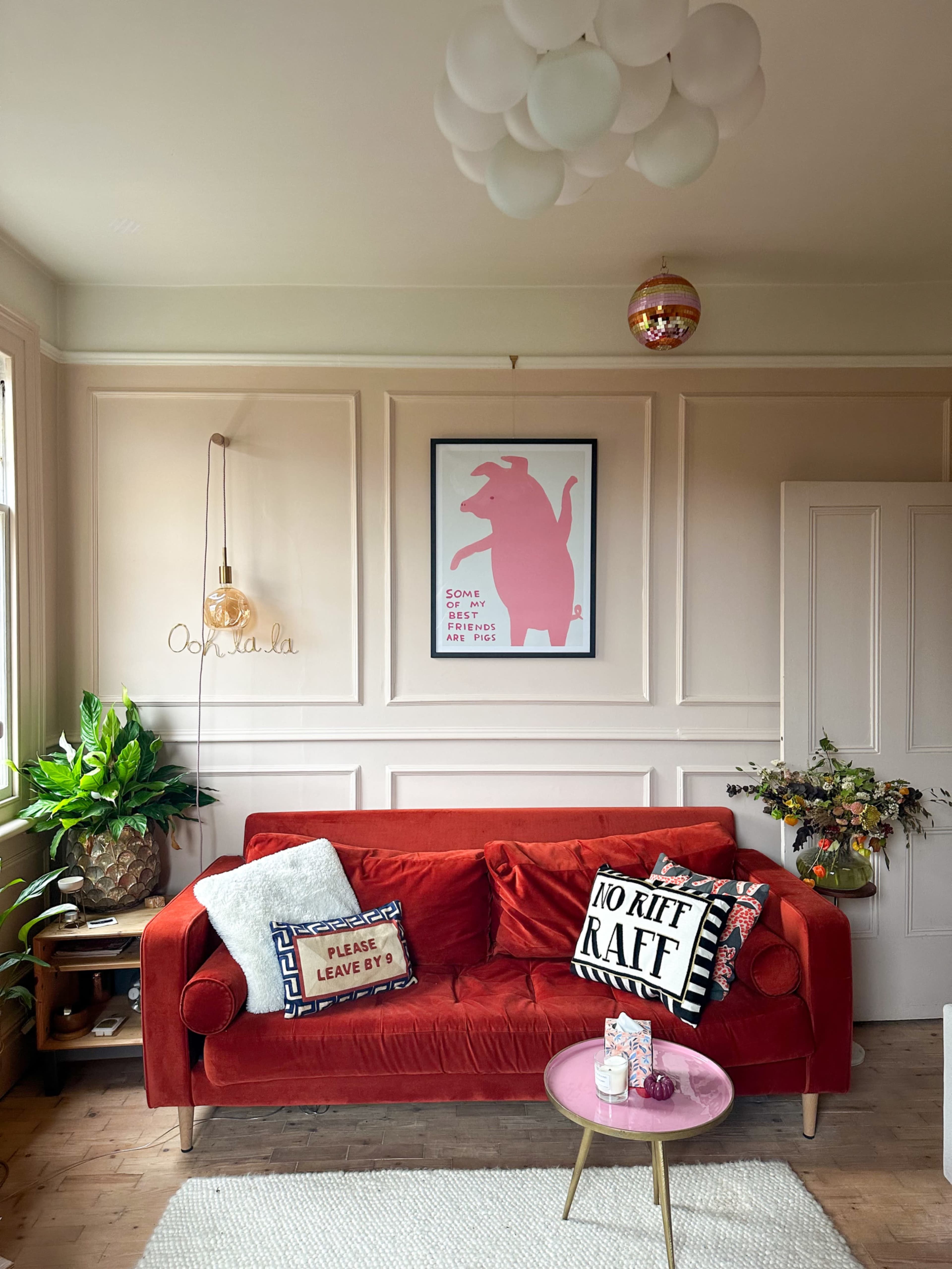 A cozy living room featuring a red sofa adorned with decorative pillows, a pink artwork on the wall, and a small round coffee table.