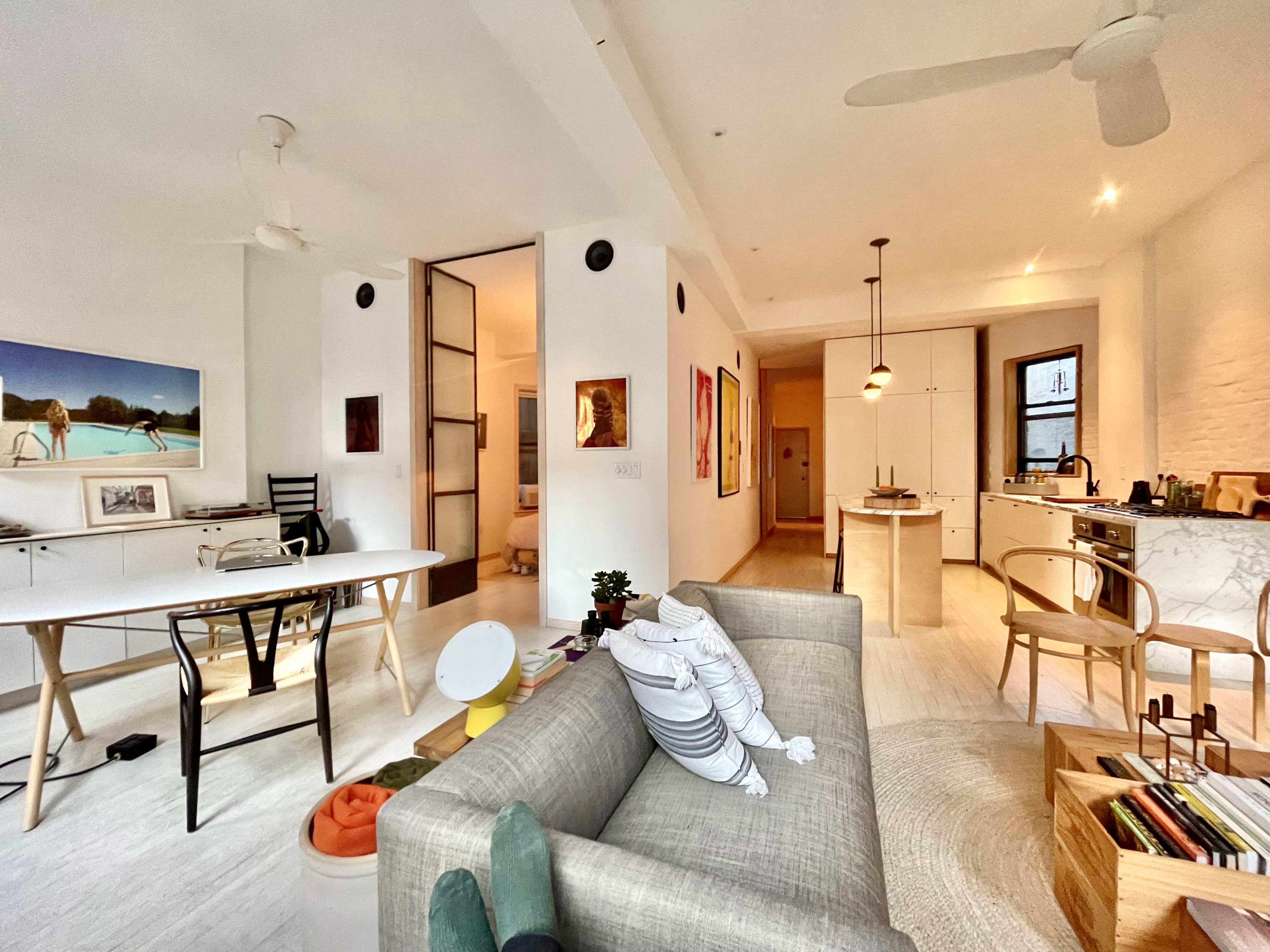 The image shows a modern, open-concept living space featuring a dining area, kitchen, and workspace arranged with minimalist furniture and decor.