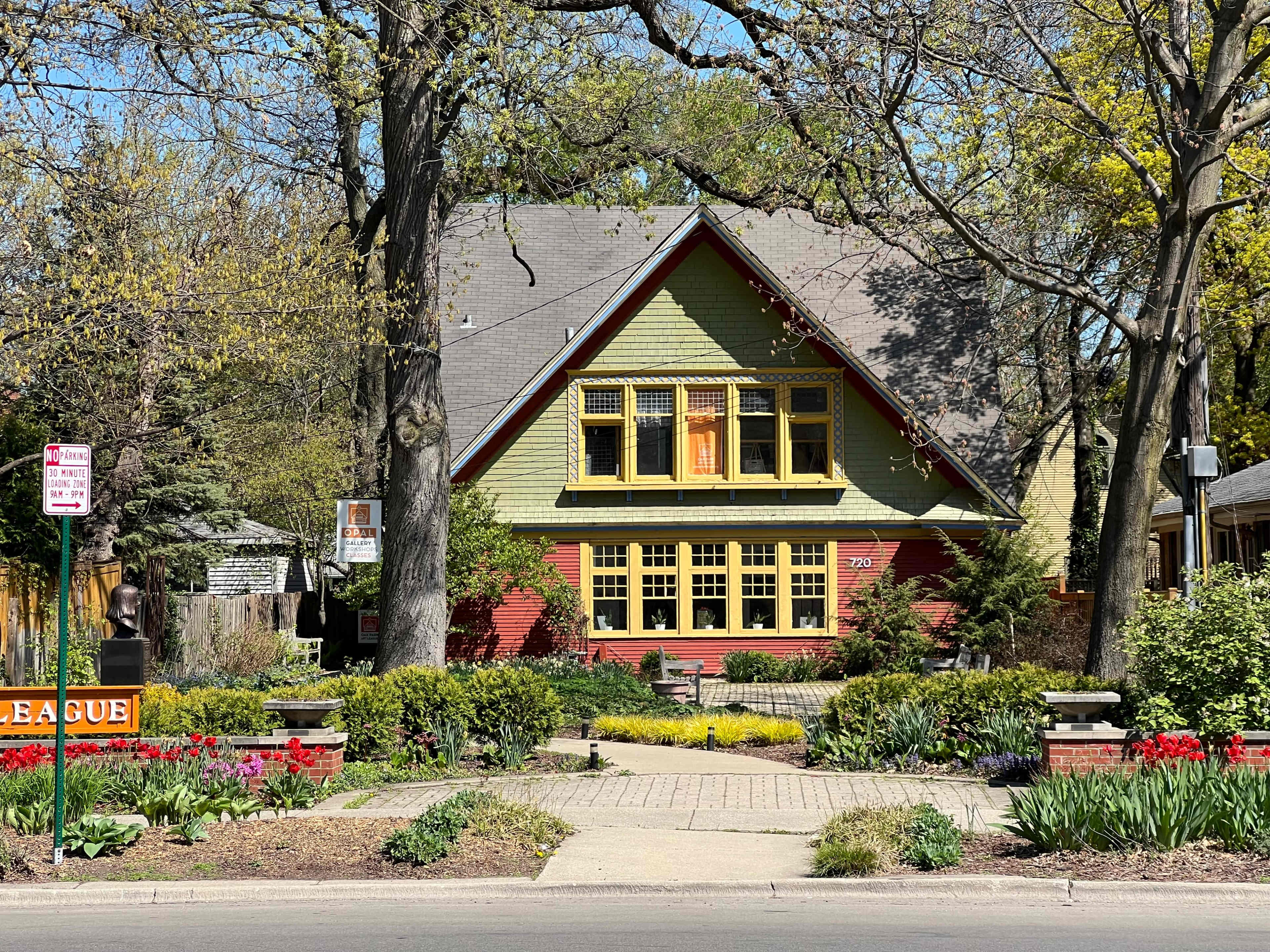 A large green and red house with yellow trim is surrounded by a well-kept garden full of flowers and trees.