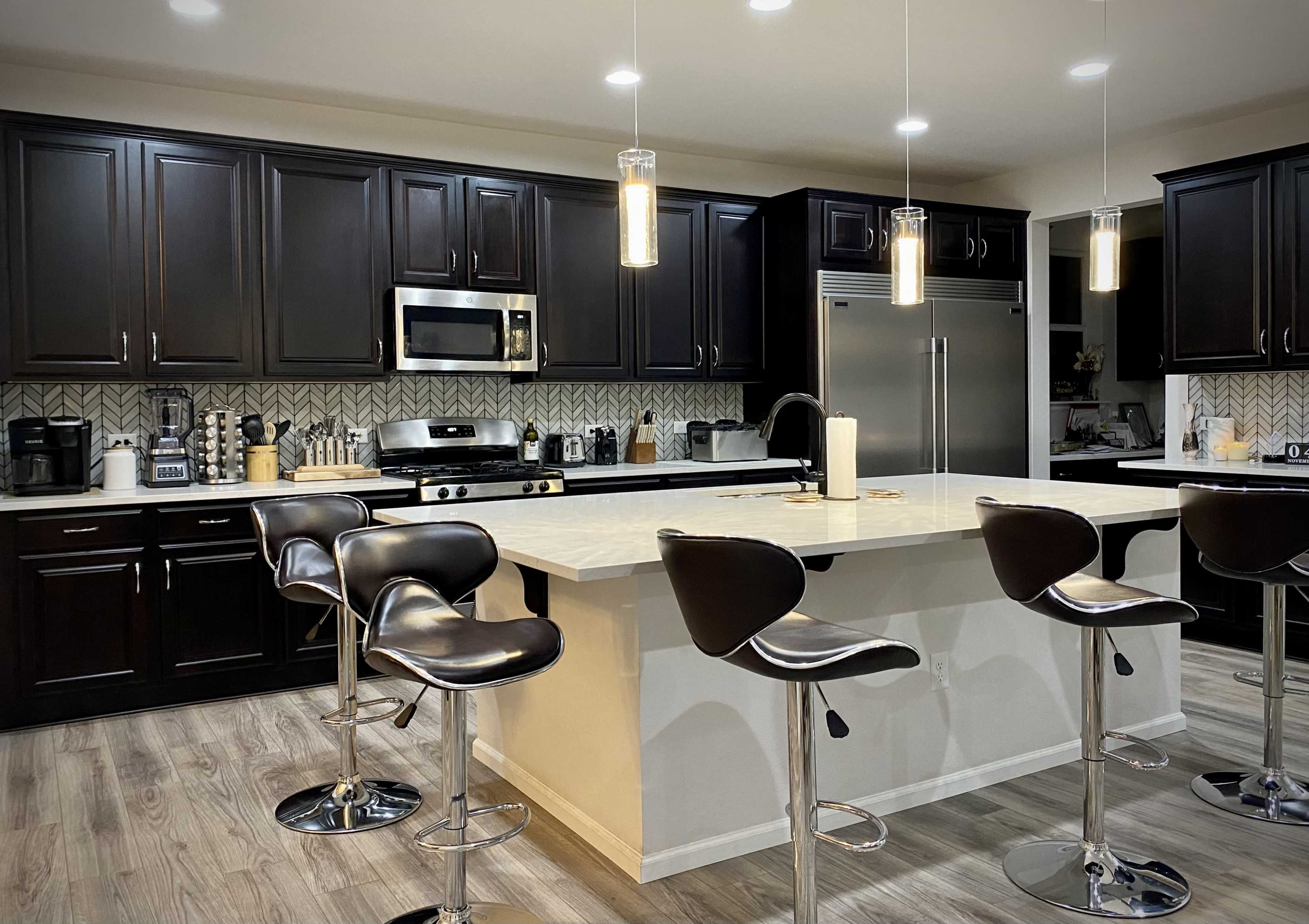 A modern kitchen with dark cabinetry, stainless steel appliances, and a central island with barstool seating.