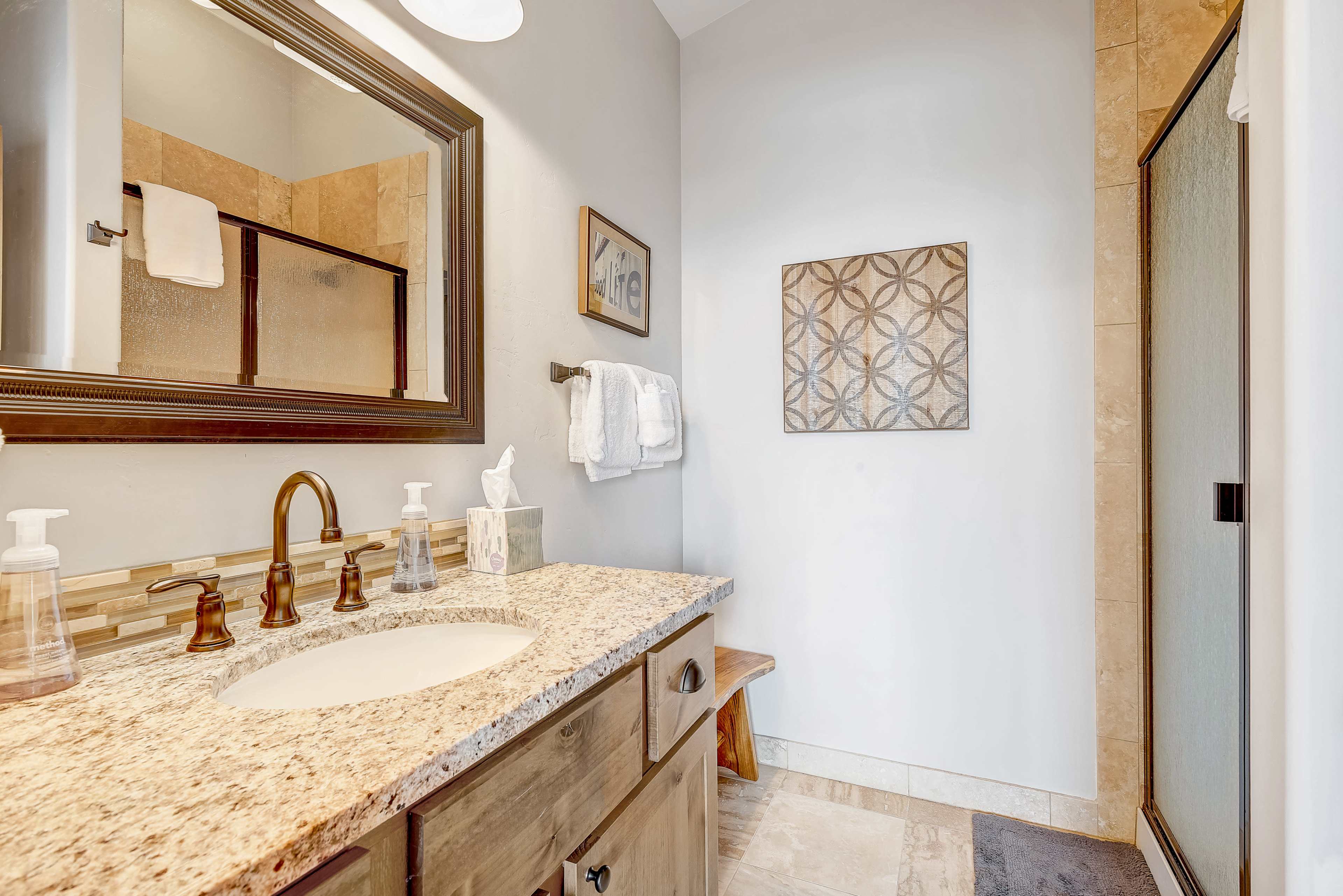 A modern bathroom featuring a granite countertop sink, a wooden cabinet, and a glass shower enclosure.