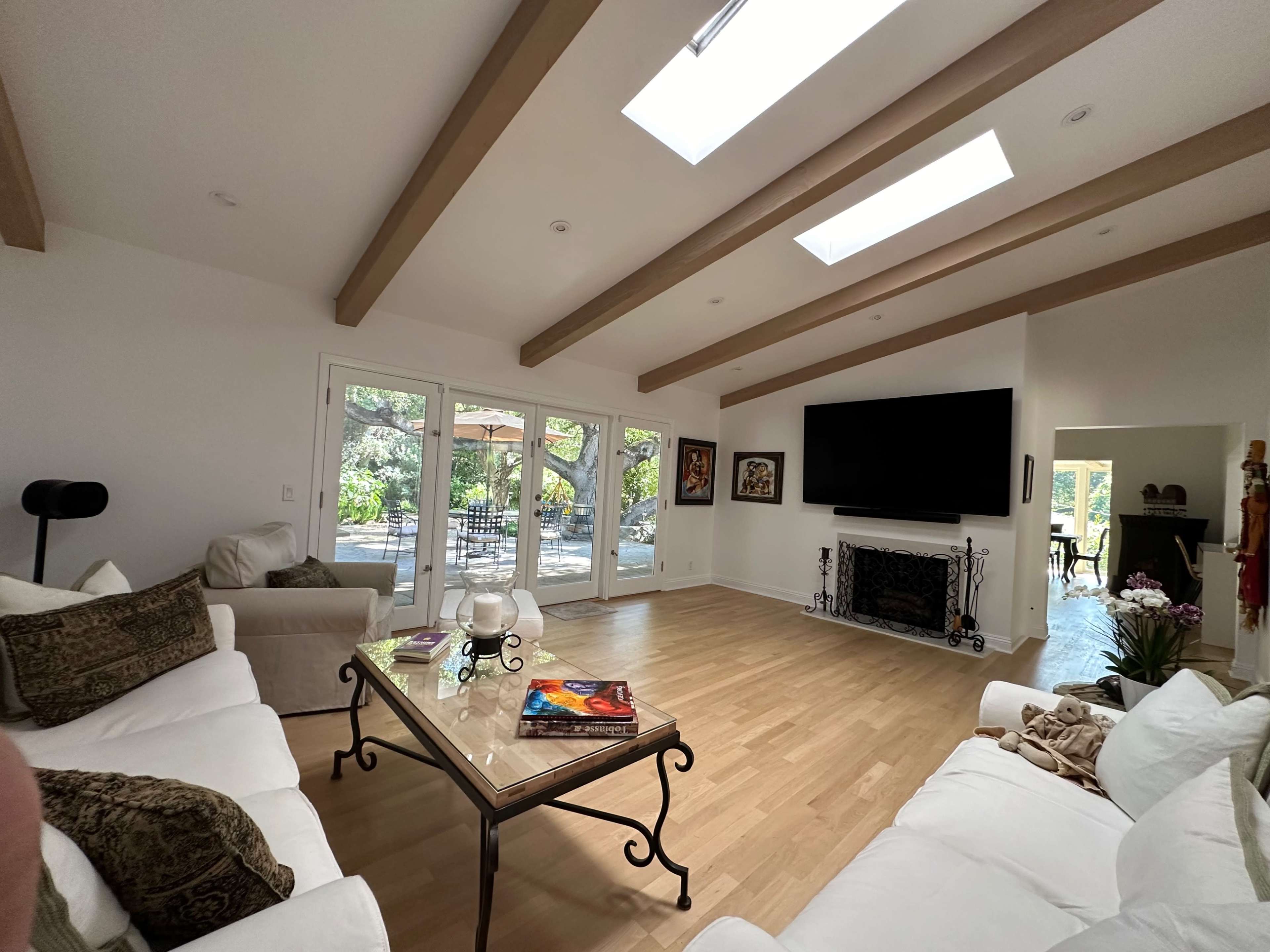 A spacious living room with wooden beams, large windows, and a wall-mounted television opposite a glass coffee table.