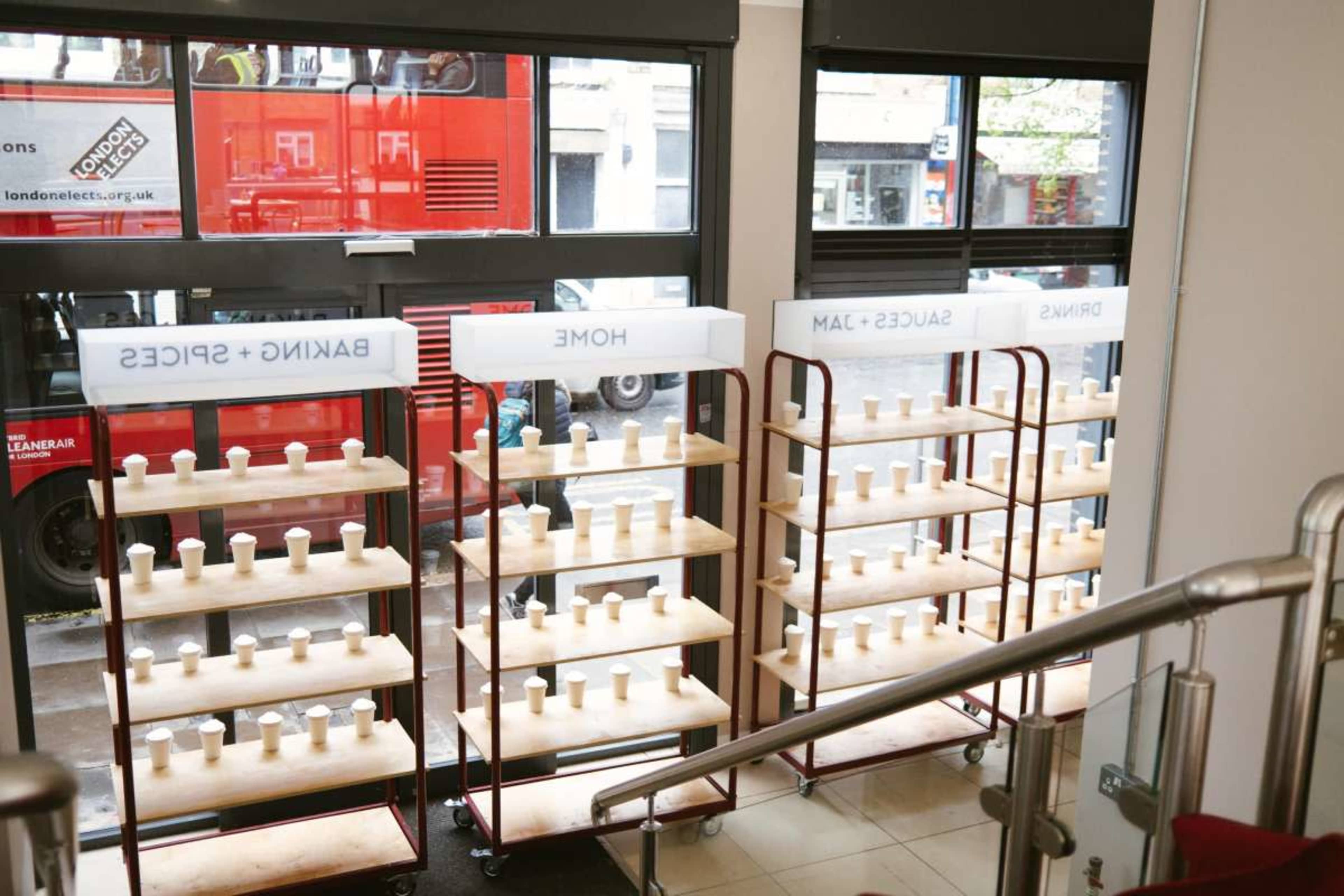 Two shelving units displaying various ceramic items in a store, with large windows revealing a red double-decker bus outside.