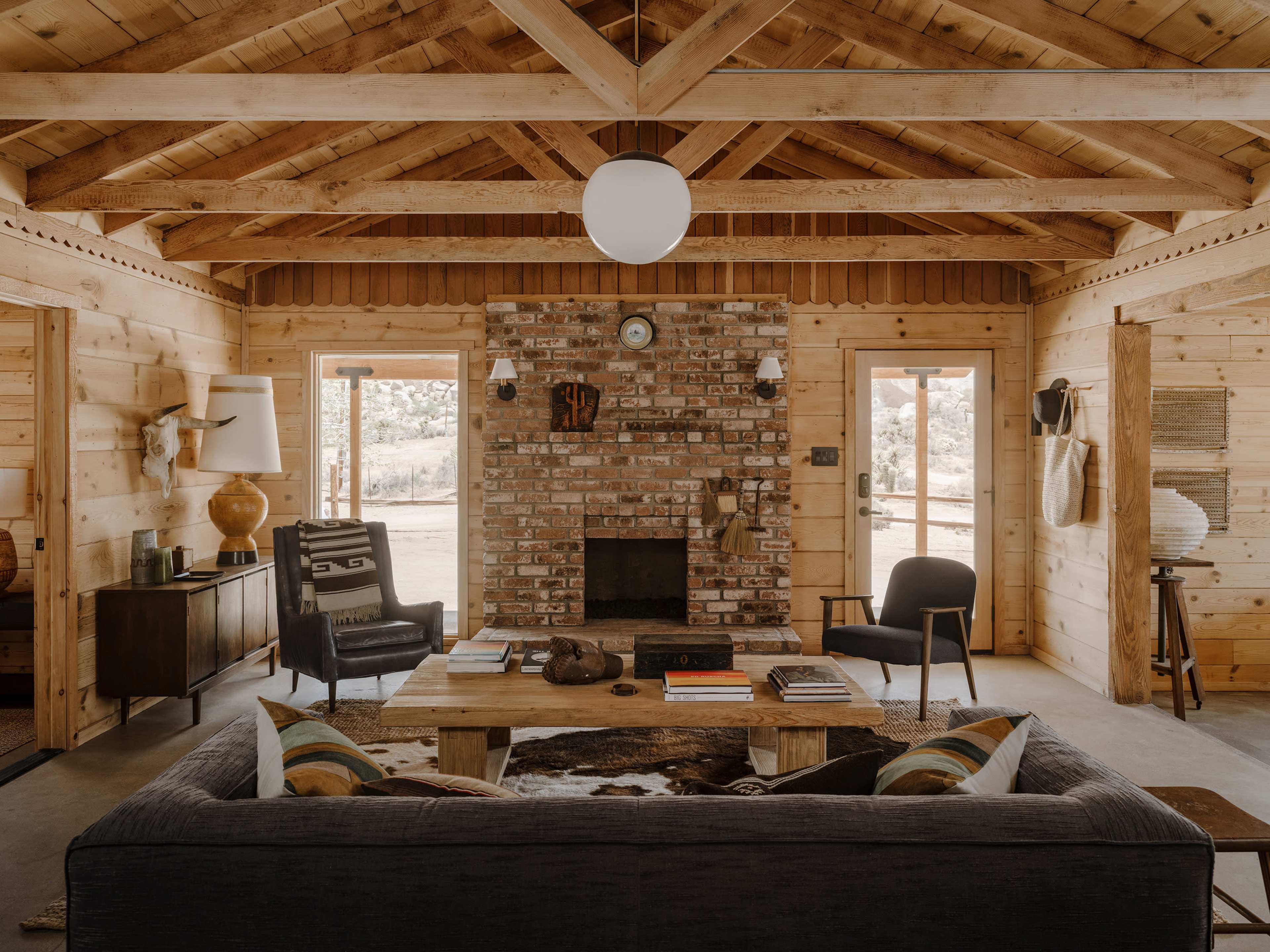 A cozy interior of a wooden cabin with a brick fireplace, a large sofa, and rustic furniture.