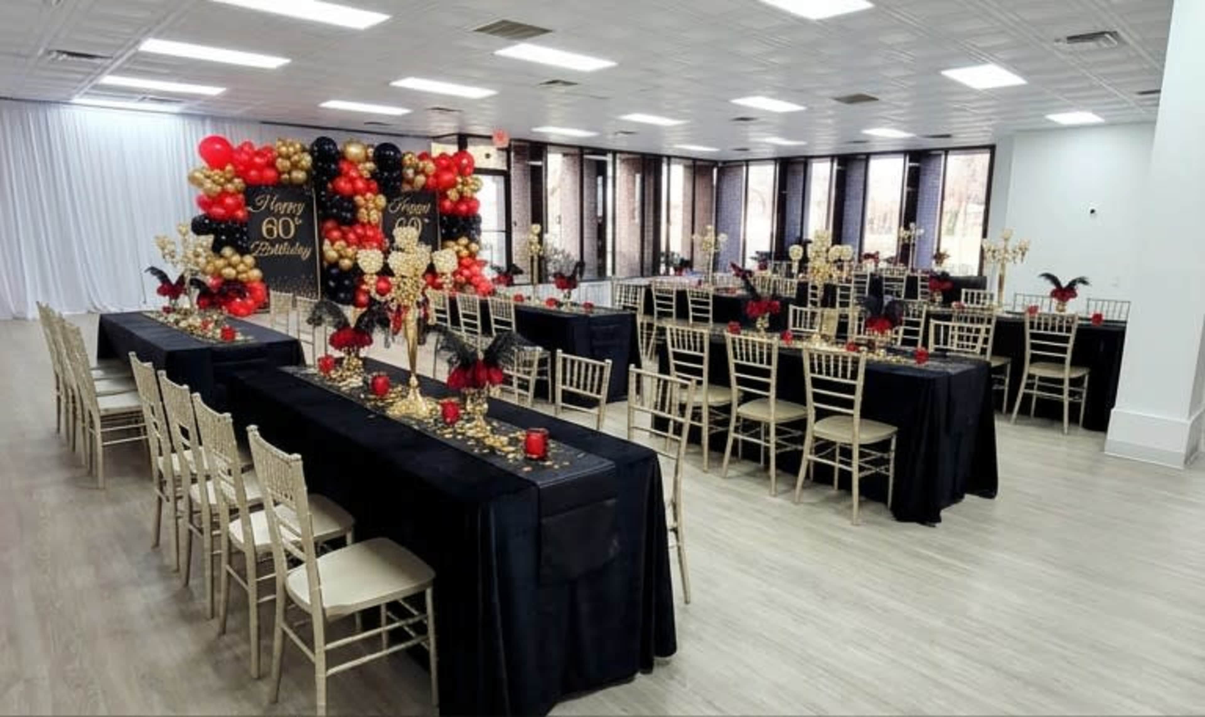 The image shows a decorated event space set up for a 60th birthday celebration, featuring black and gold tablecloths, centerpieces of balloons, and candelabras on each table.
