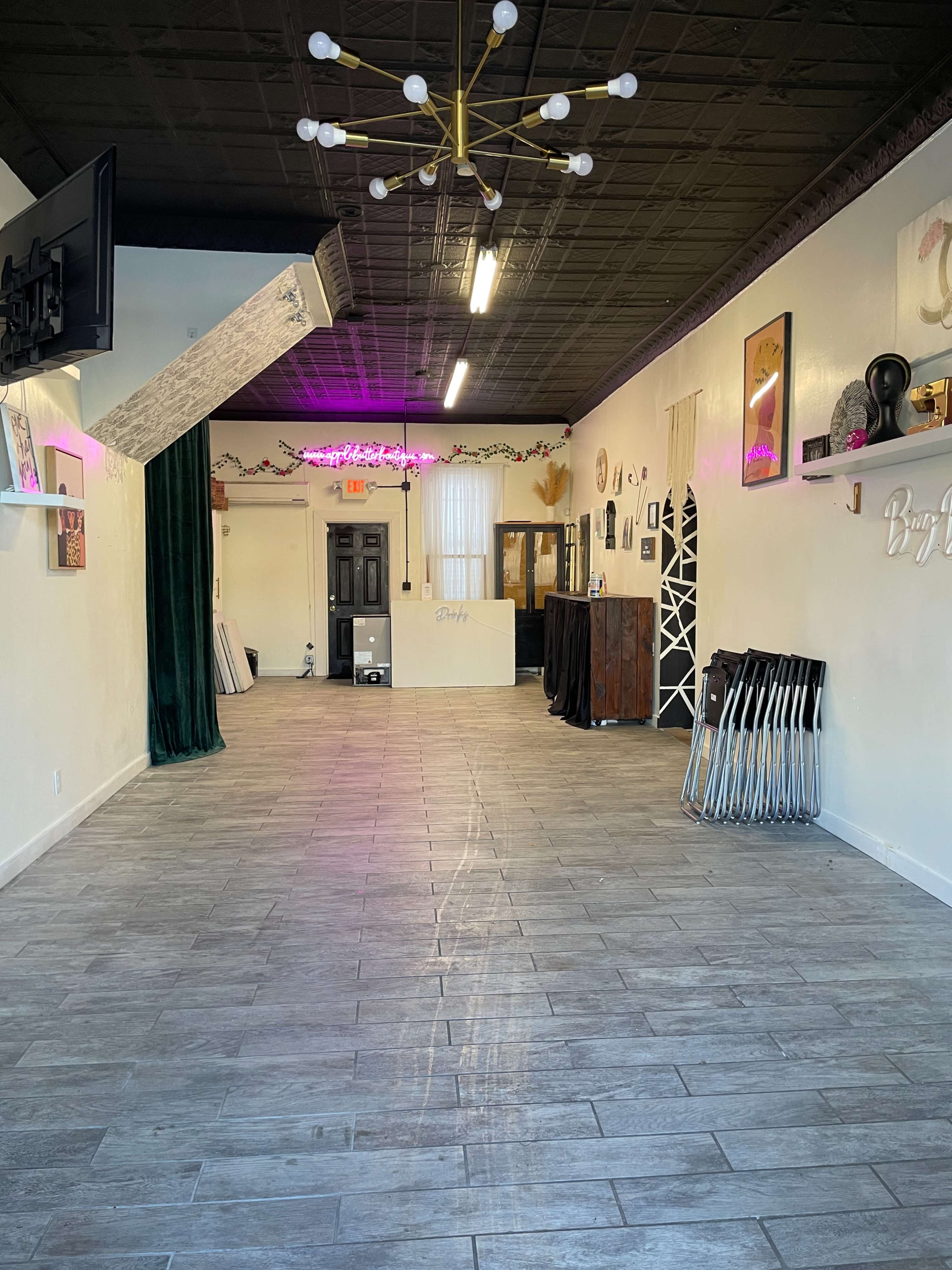 The image shows an empty, well-lit indoor space with a tiled floor, green curtains on one side, and various decor items on the walls.