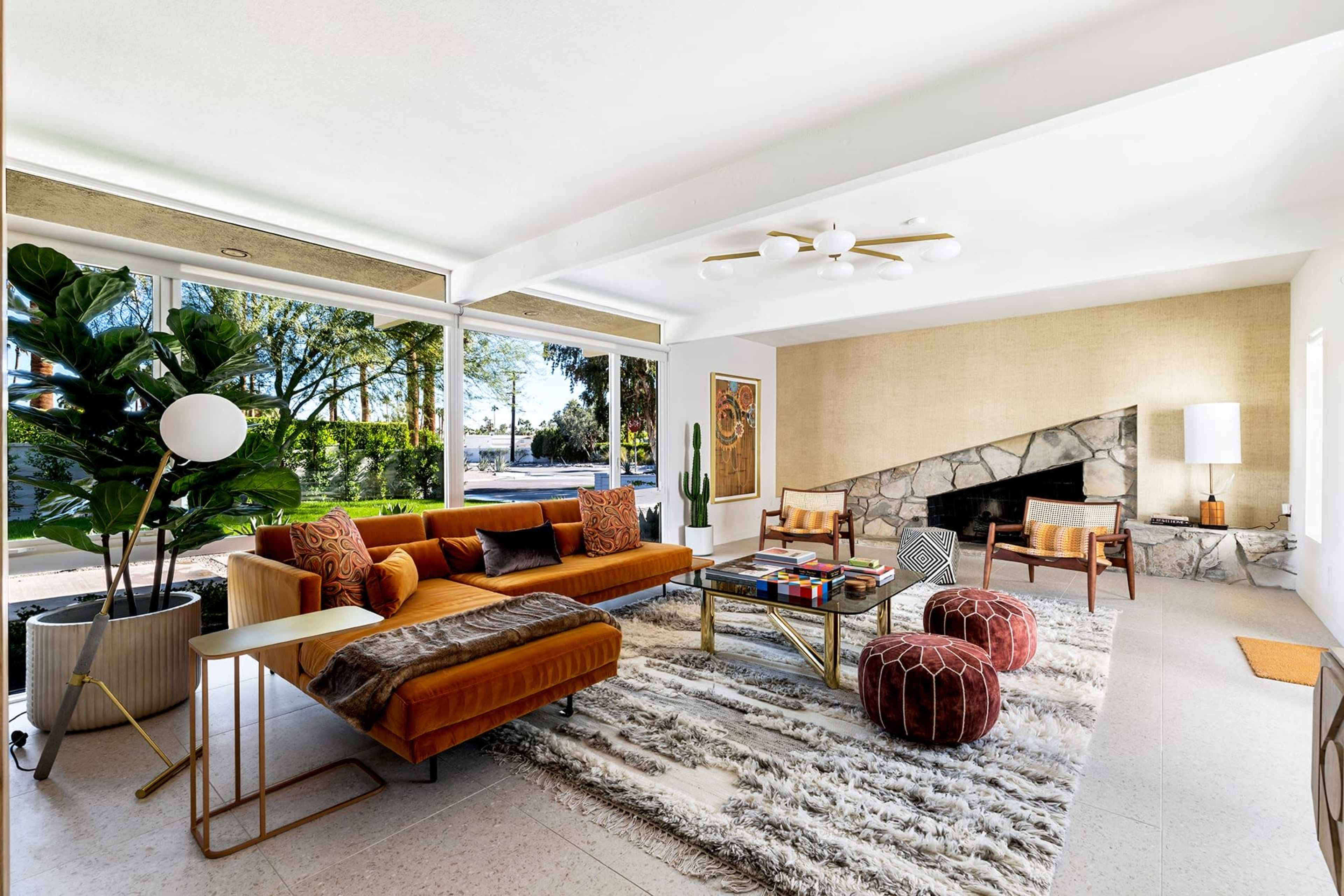 A modern living room features a sectional sofa, a stone fireplace, and large windows overlooking a green landscape.