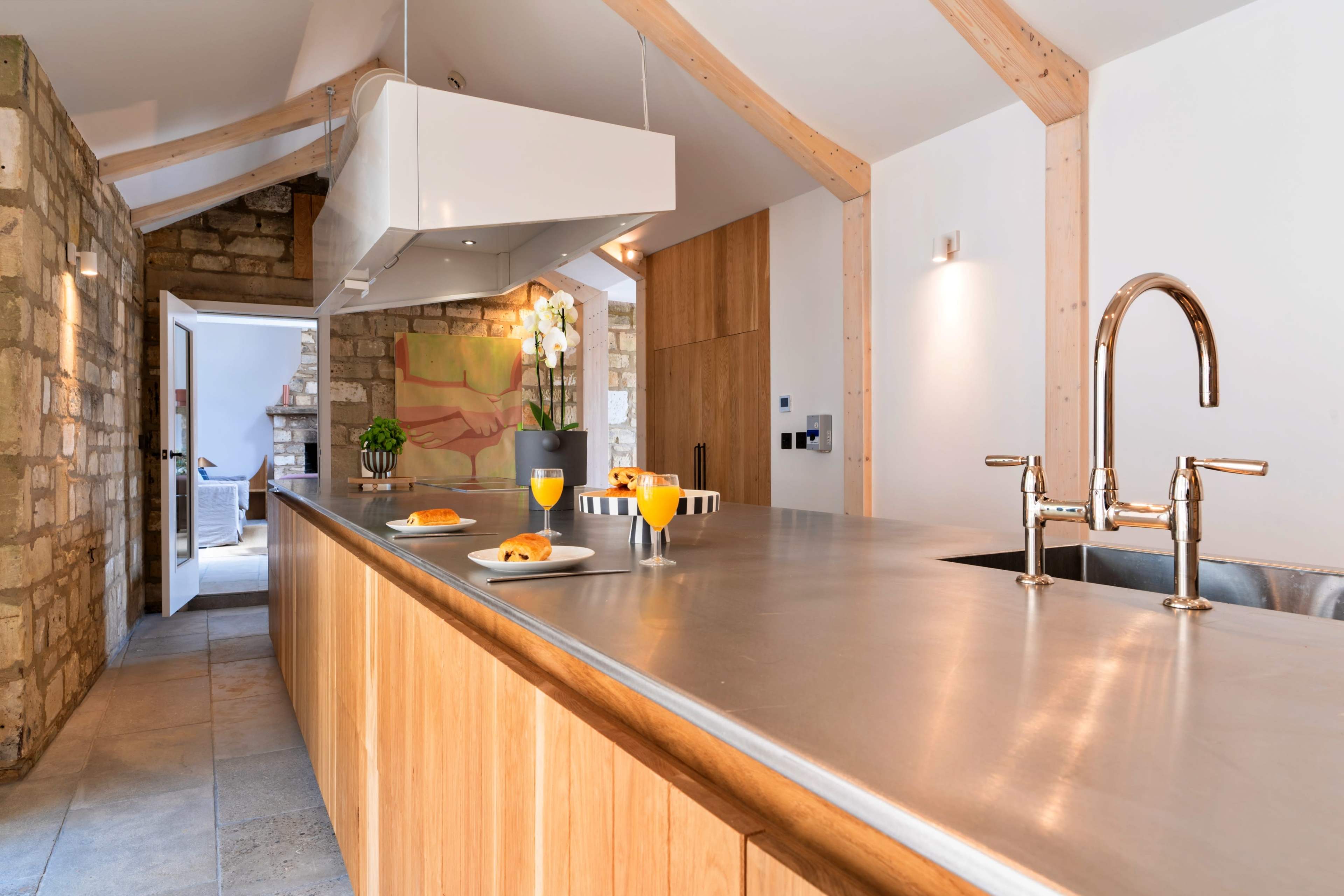 A spacious kitchen features a central wooden island with a metallic countertop, equipped with modern appliances and breakfast items, surrounded by stone and wooden accents.