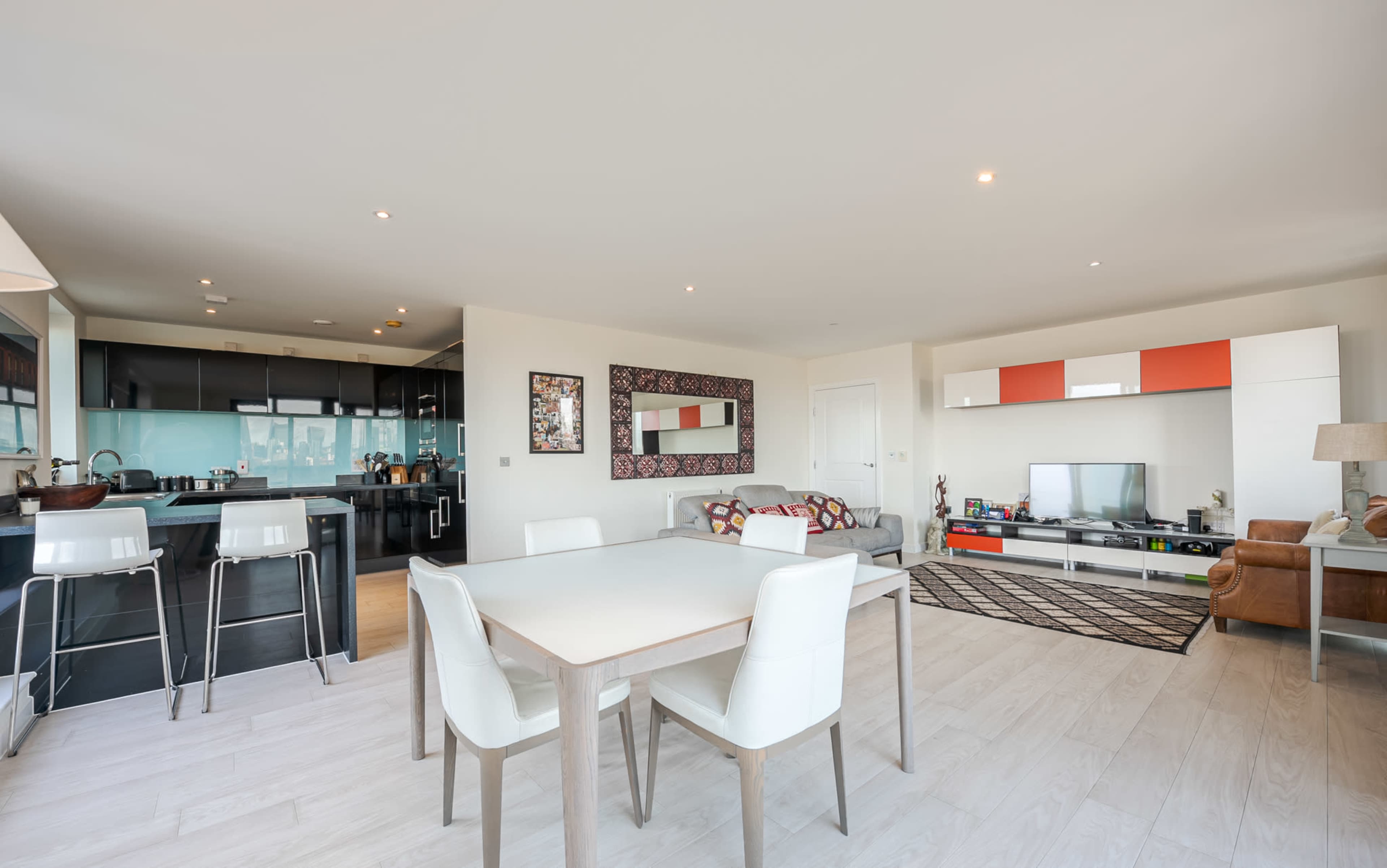 The image shows a modern open-concept living and dining area featuring a dining table, chairs, a living room with a sofa, and a television.