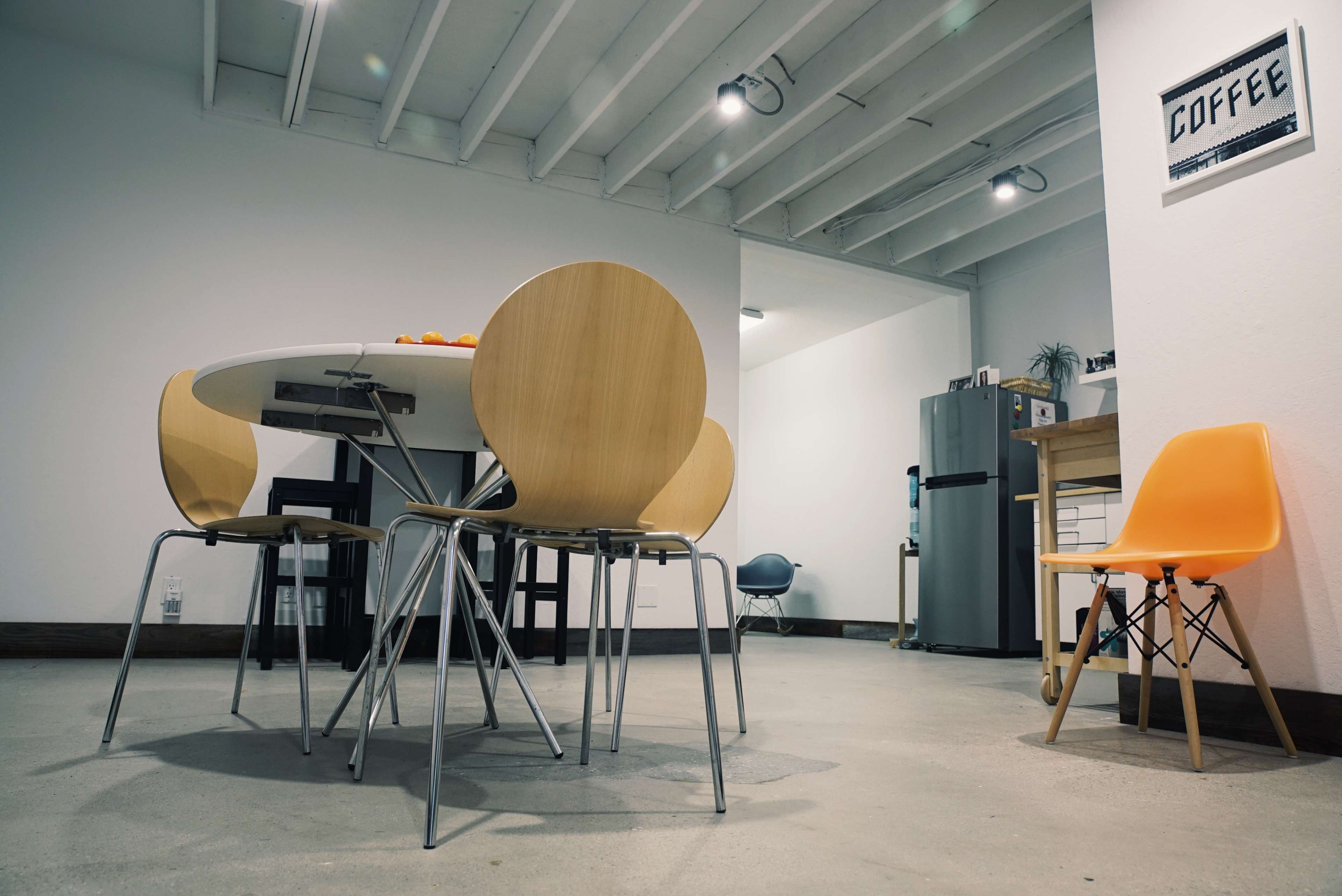 A modern kitchen with a circular table surrounded by wooden chairs, a refrigerator, and a small orange chair in the corner.