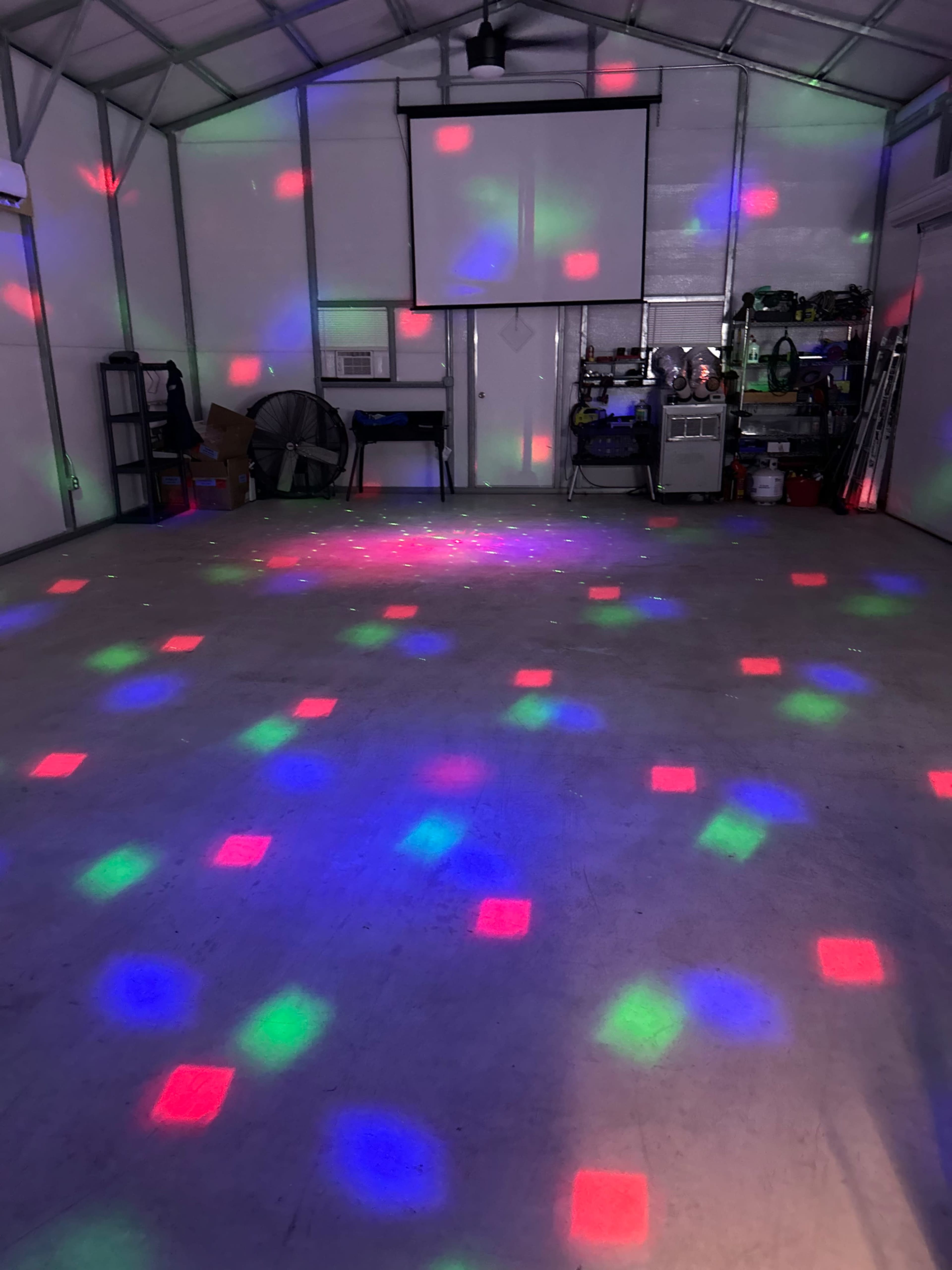The interior of a garage features a concrete floor illuminated with colorful lights projecting patterns on the surface.