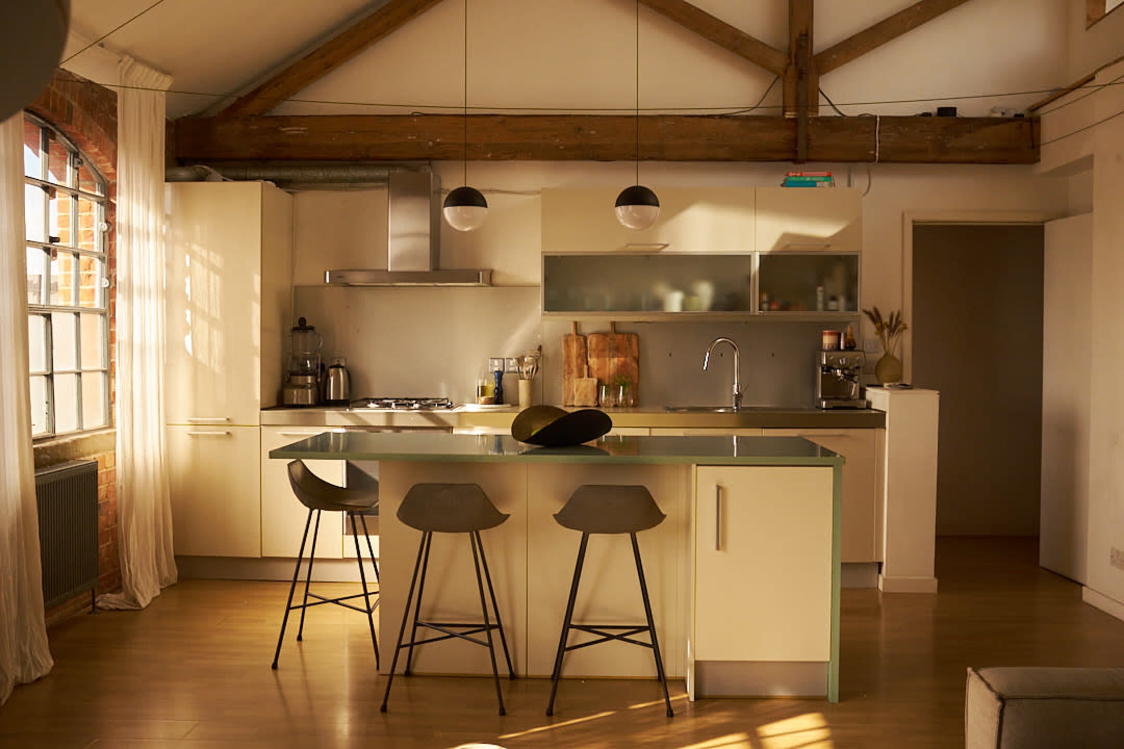 A modern kitchen features an island with stools, stainless steel appliances, and large windows illuminating the space.