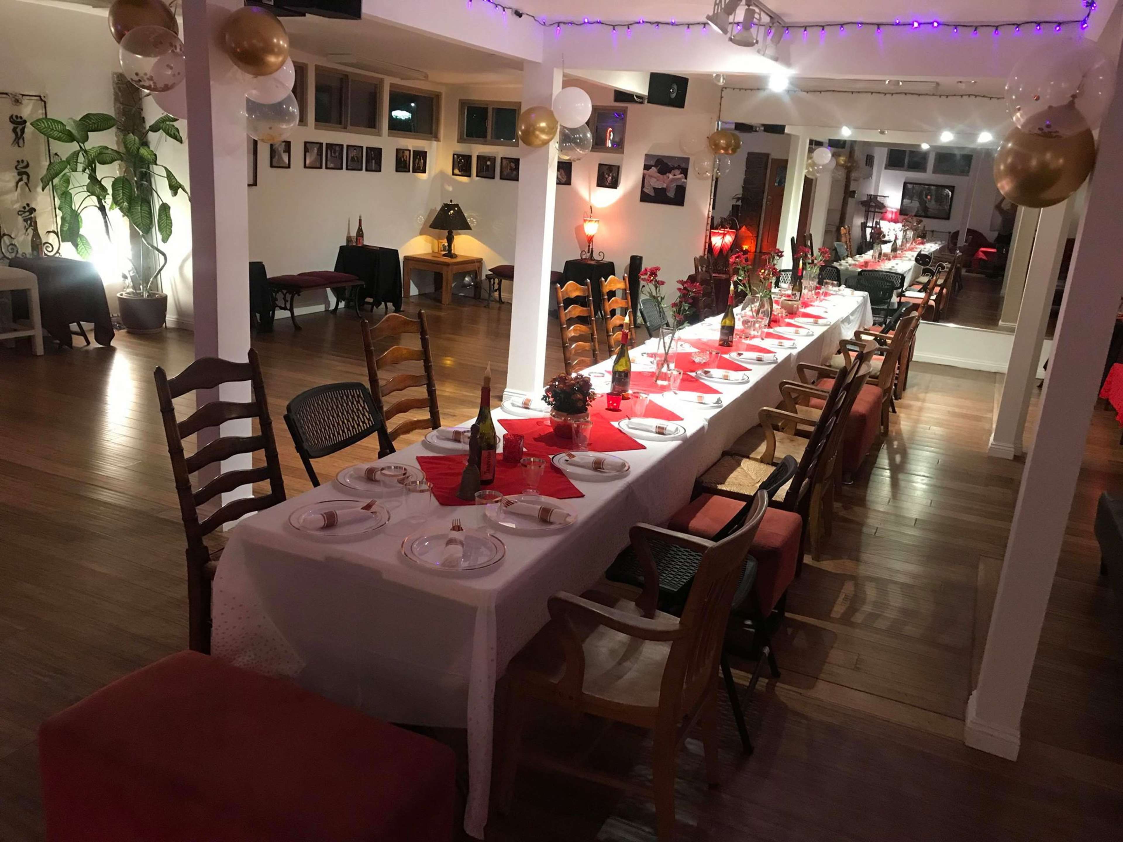 A long dining table is set with plates and glasses in a warmly lit room decorated with balloons and photographs on the walls.