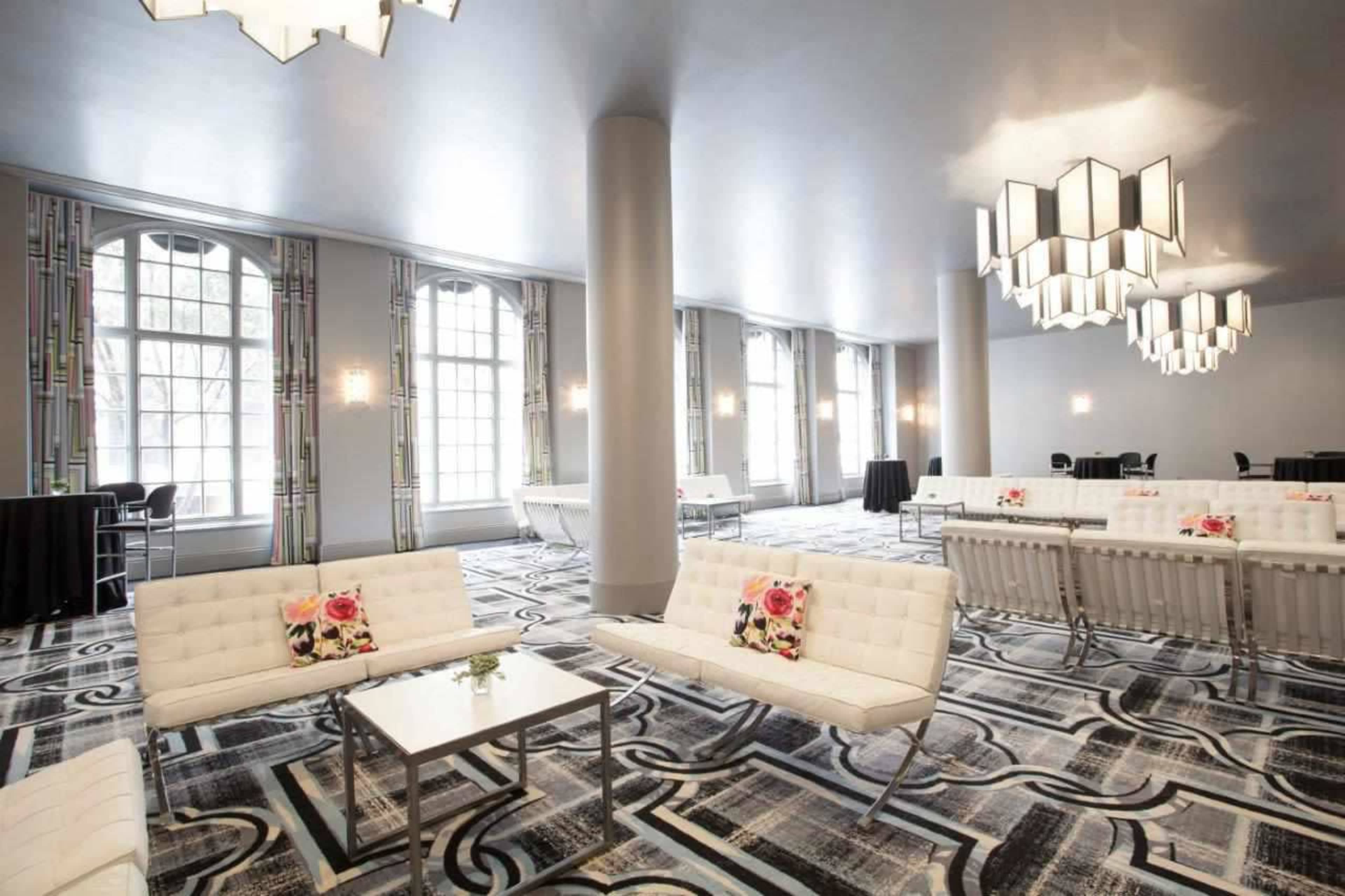 A spacious event room with modern seating, geometric patterned carpeting, and decorative lighting fixtures.