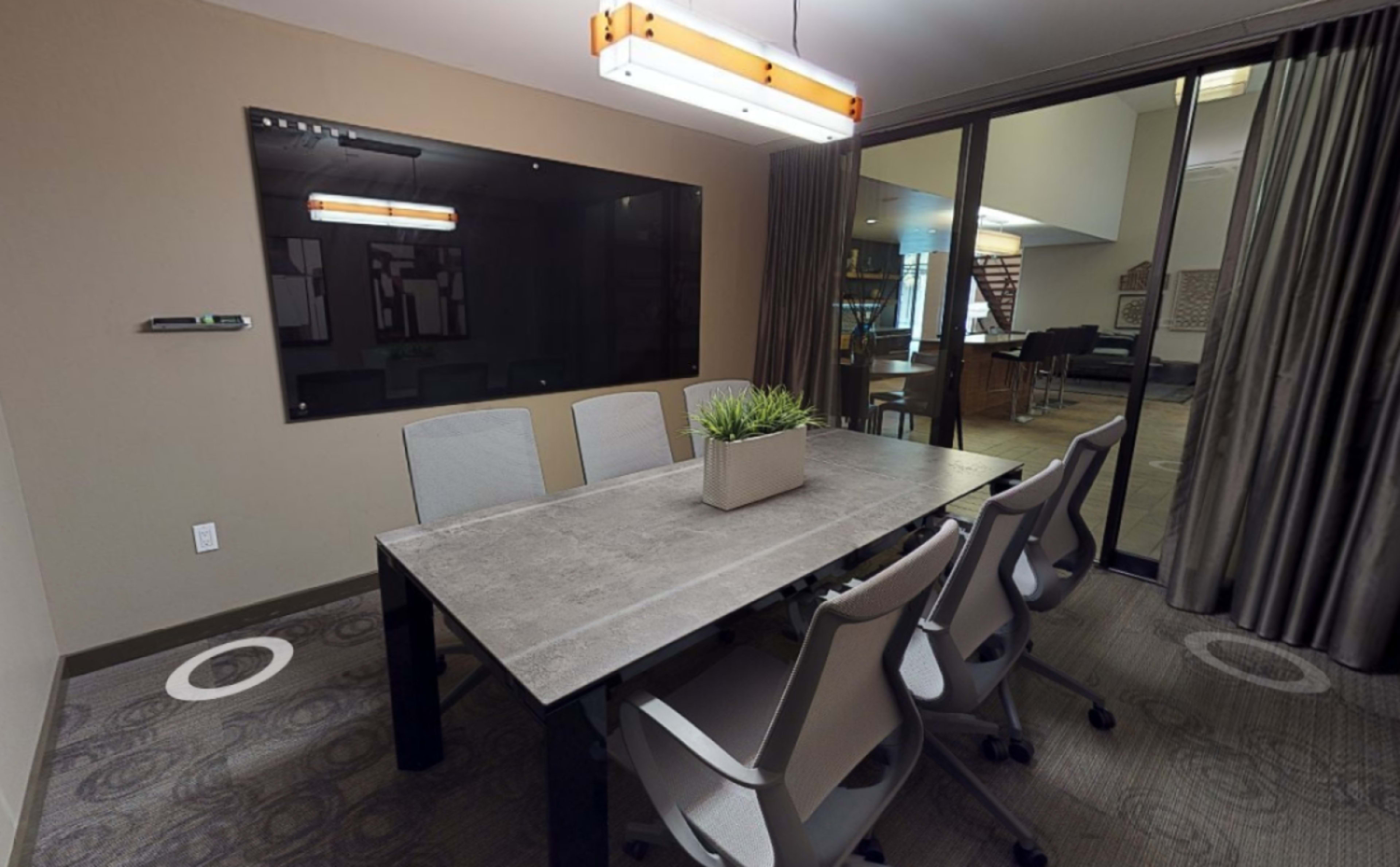 The image shows a modern conference room with a rectangular table, six chairs, a wall-mounted screen, and a large window with curtains.