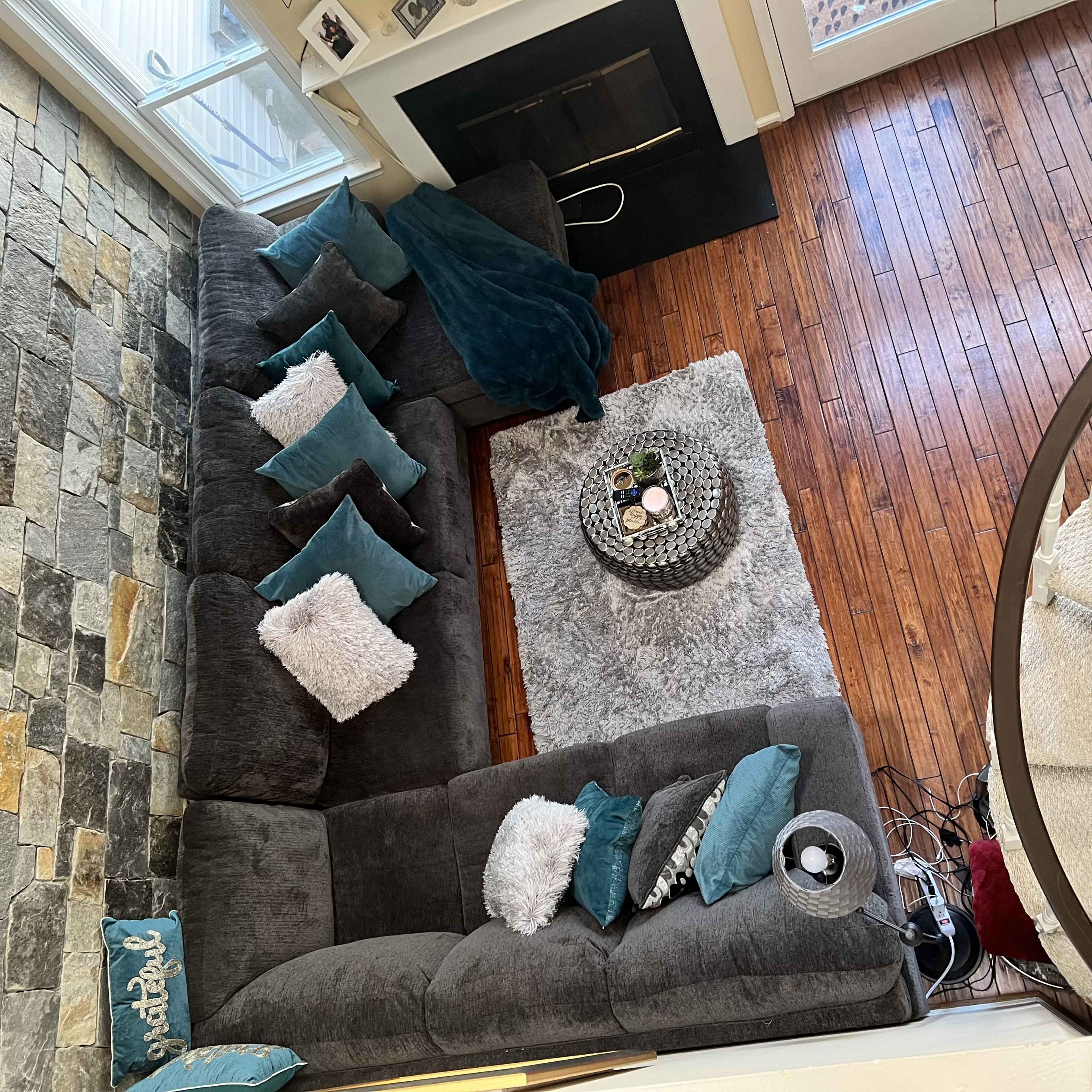 A spacious living area with a large gray sectional sofa, a round coffee table on a plush rug, and a stone fireplace.