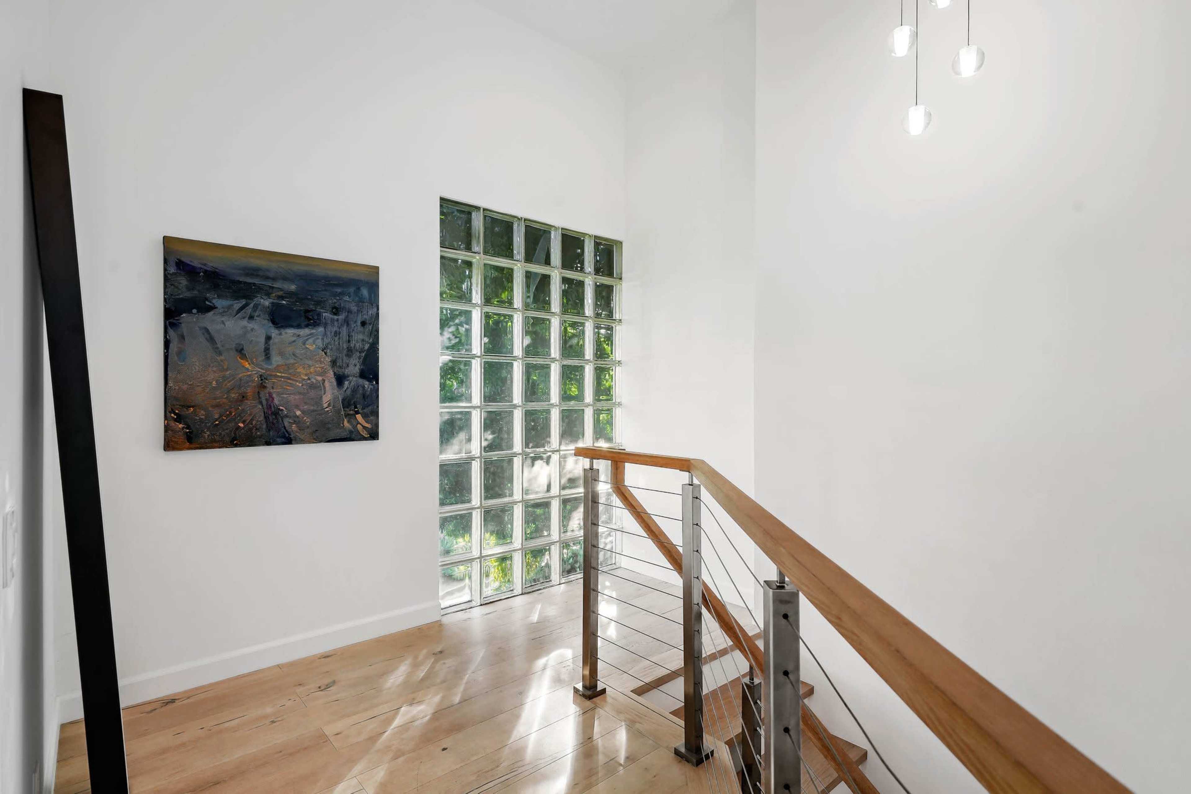 A bright stairway features a glass block wall, wooden railing, and an abstract painting on the wall.