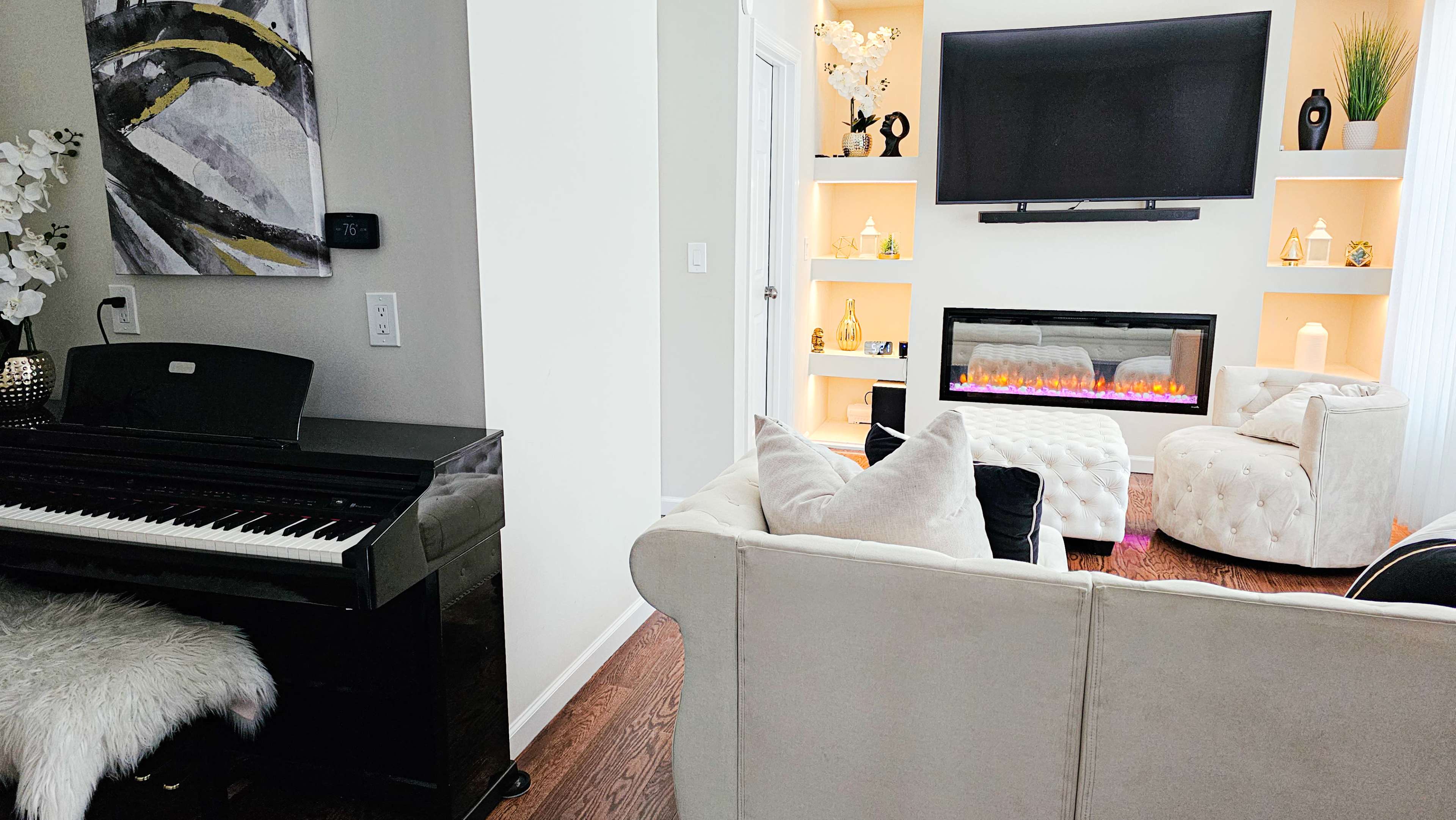 A modern living room with a piano on the left, a cozy couch, and an electric fireplace beneath a wall-mounted television.