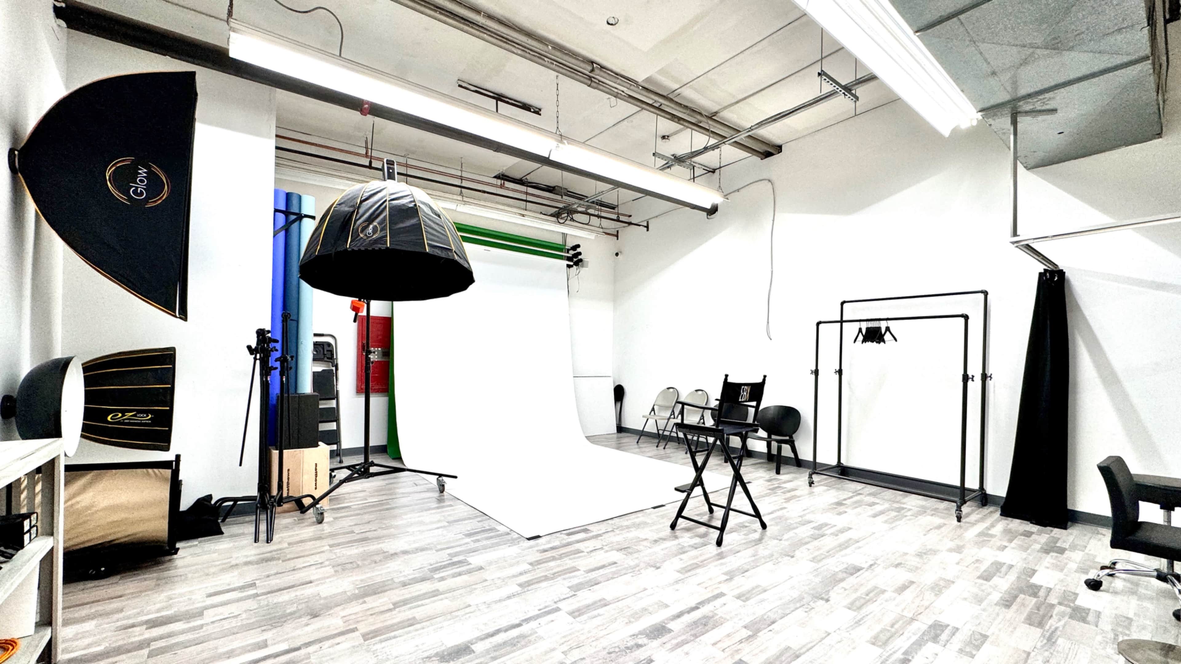 A photography studio with a white backdrop, lighting equipment, a director's chair, and various props arranged neatly in the space.