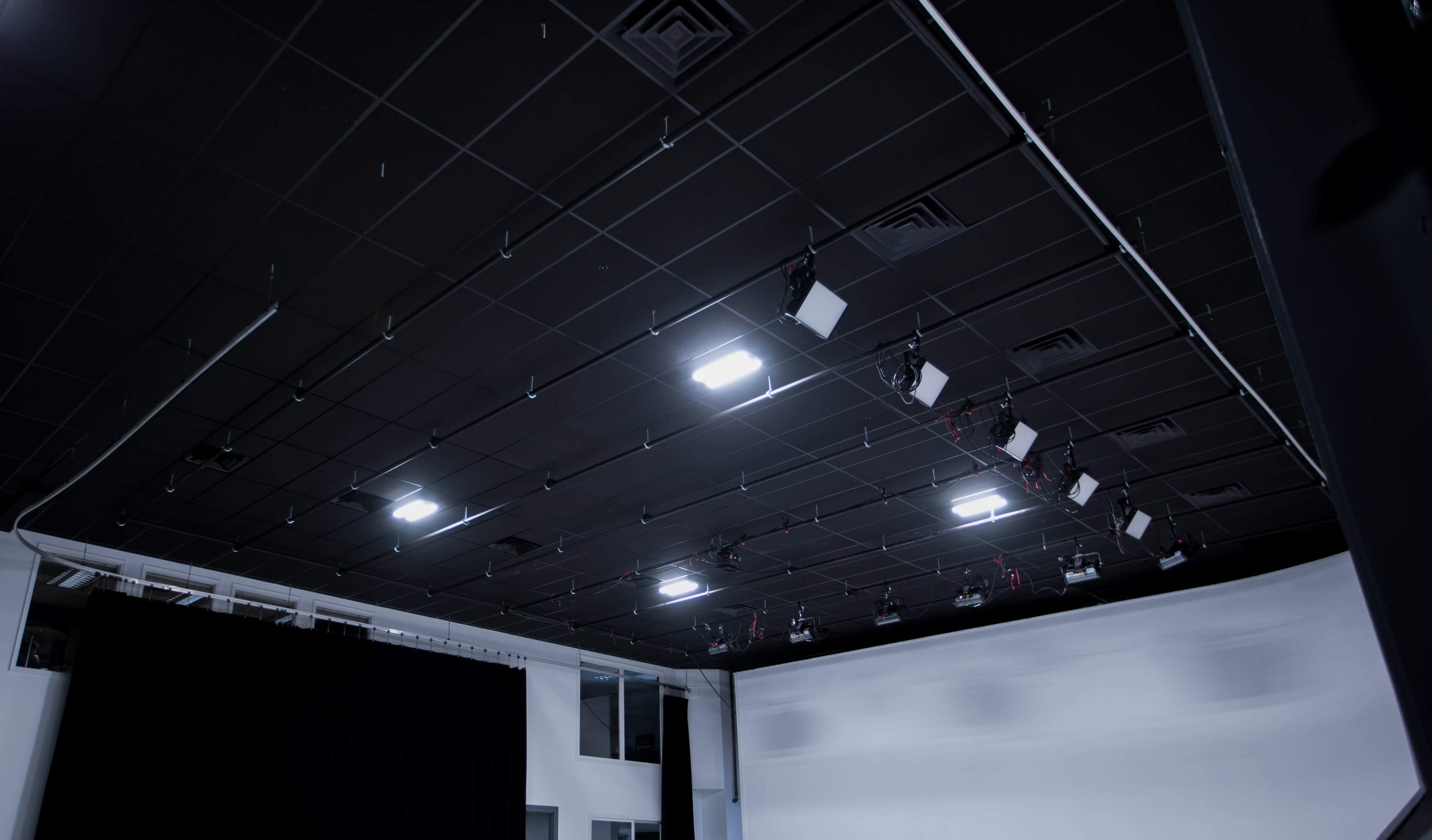 The image shows a spacious studio with a black ceiling featuring overhead lights and a white backdrop on one wall.