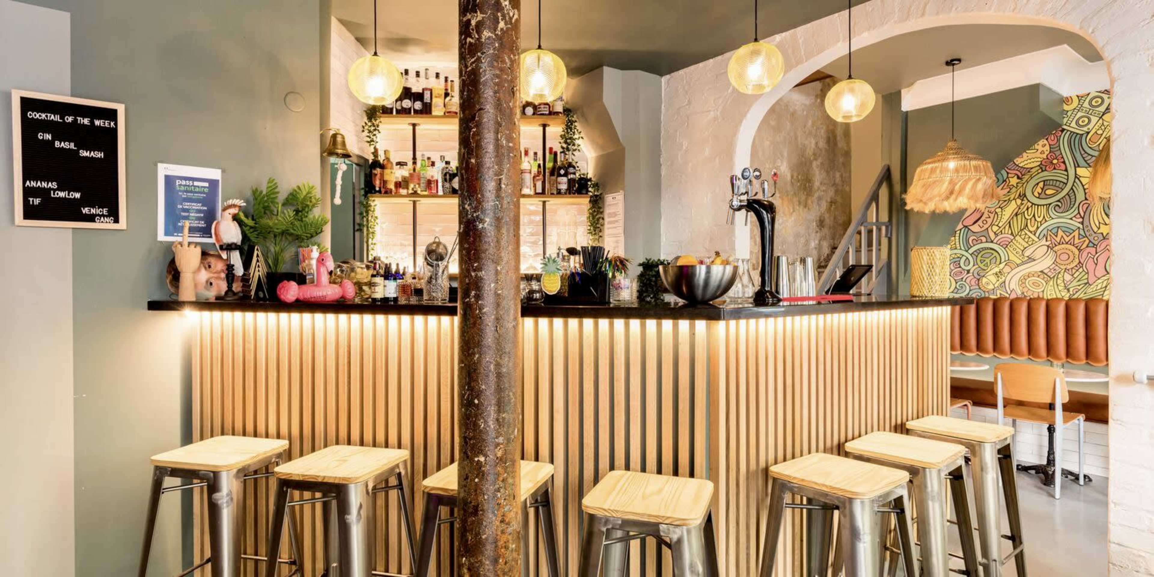A bar area features a sleek counter with wooden paneling, adorned with pendant lights, and several metal stools arranged in front.
