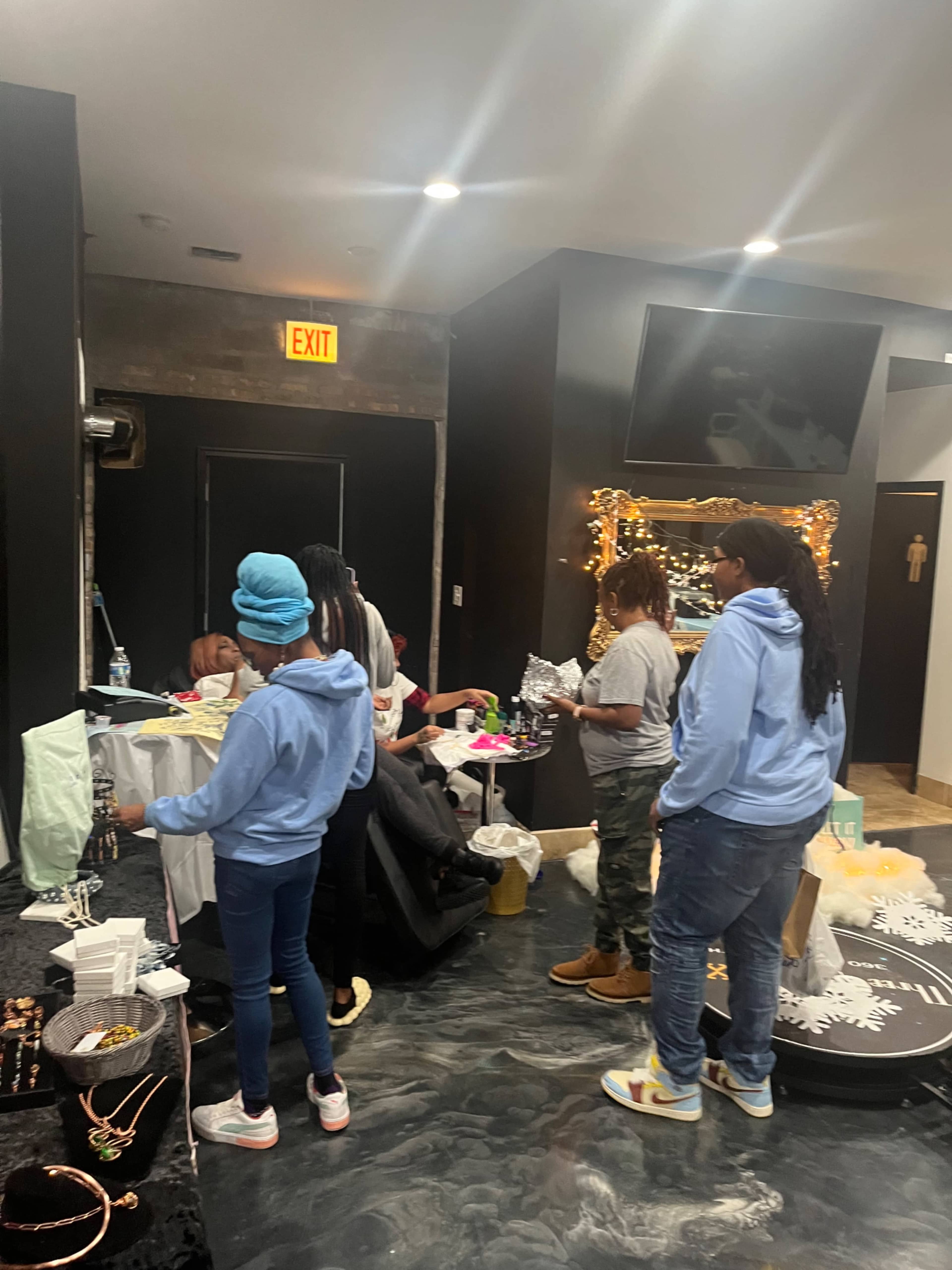 A group of people are interacting and organizing items at a small market or pop-up shop event.