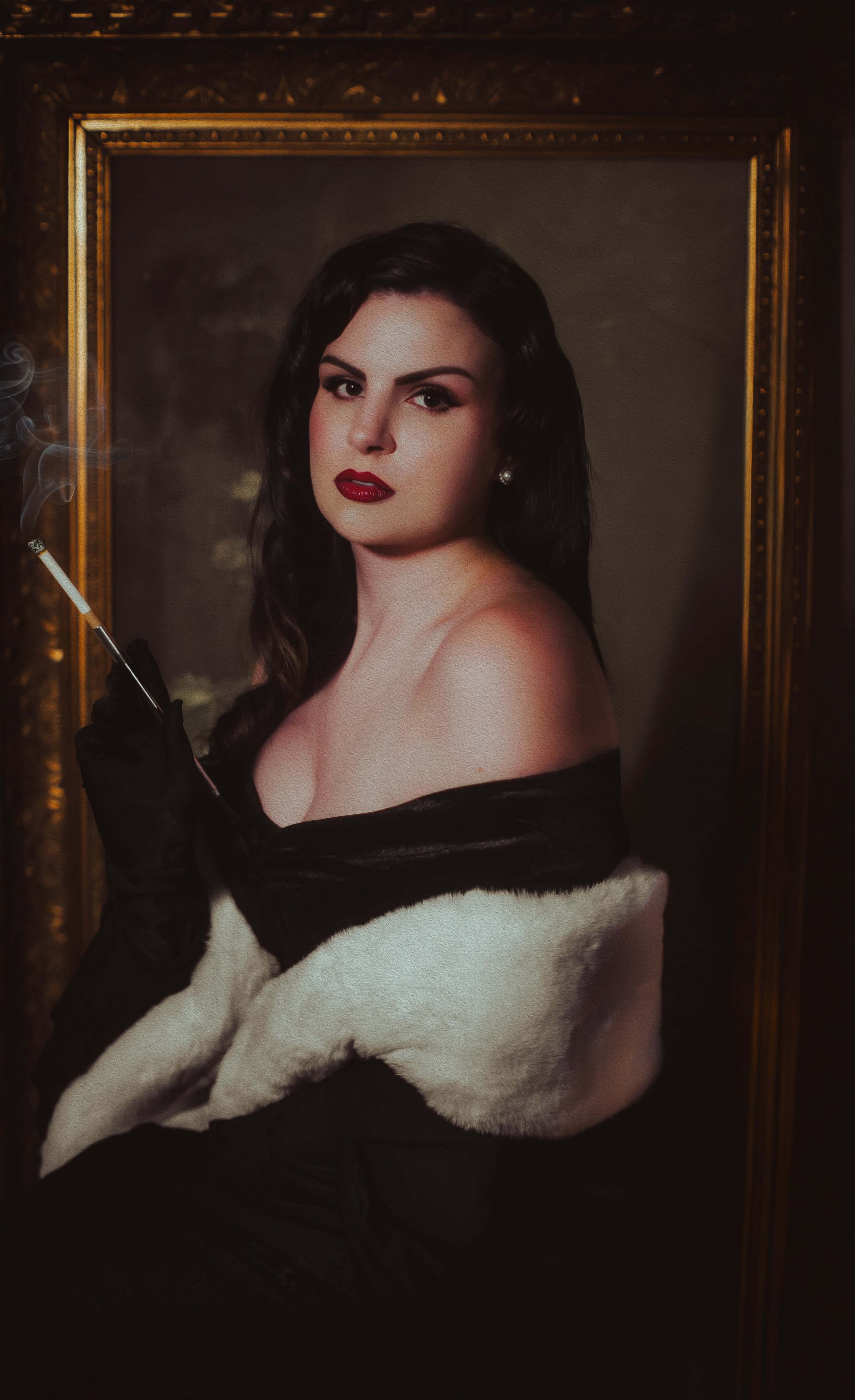 A woman with long dark hair, dressed in a black gown and white fur stole, holds a cigarette while sitting in front of a gold-framed portrait.