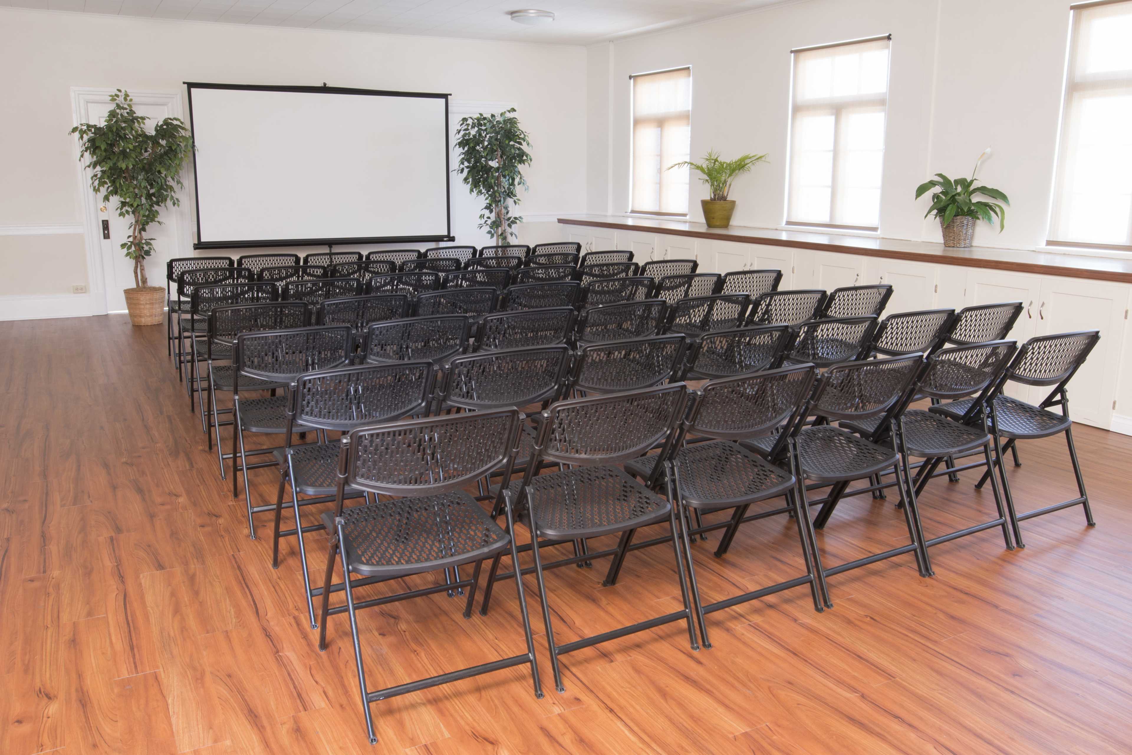 A room set up with rows of black folding chairs facing a blank projection screen.