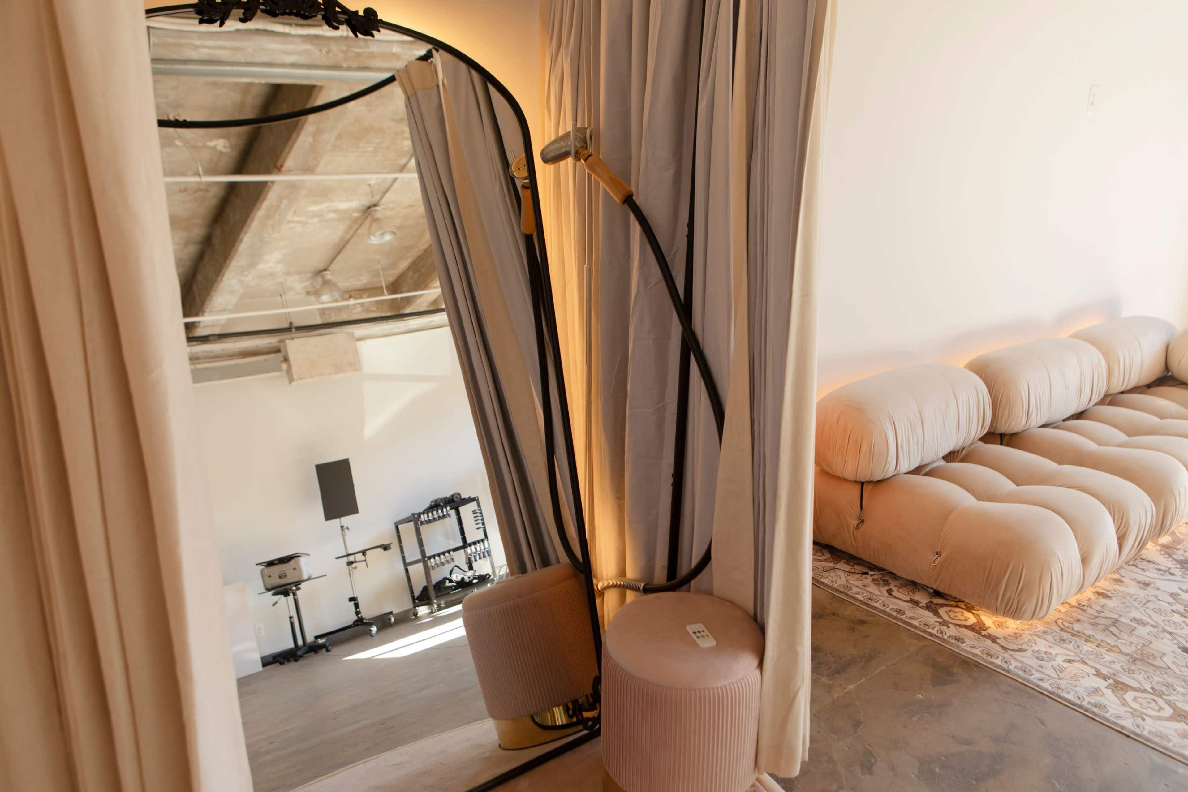 The image shows a cozy interior space featuring a curved mirror, beige curtains, and a plush, light-colored sofa.