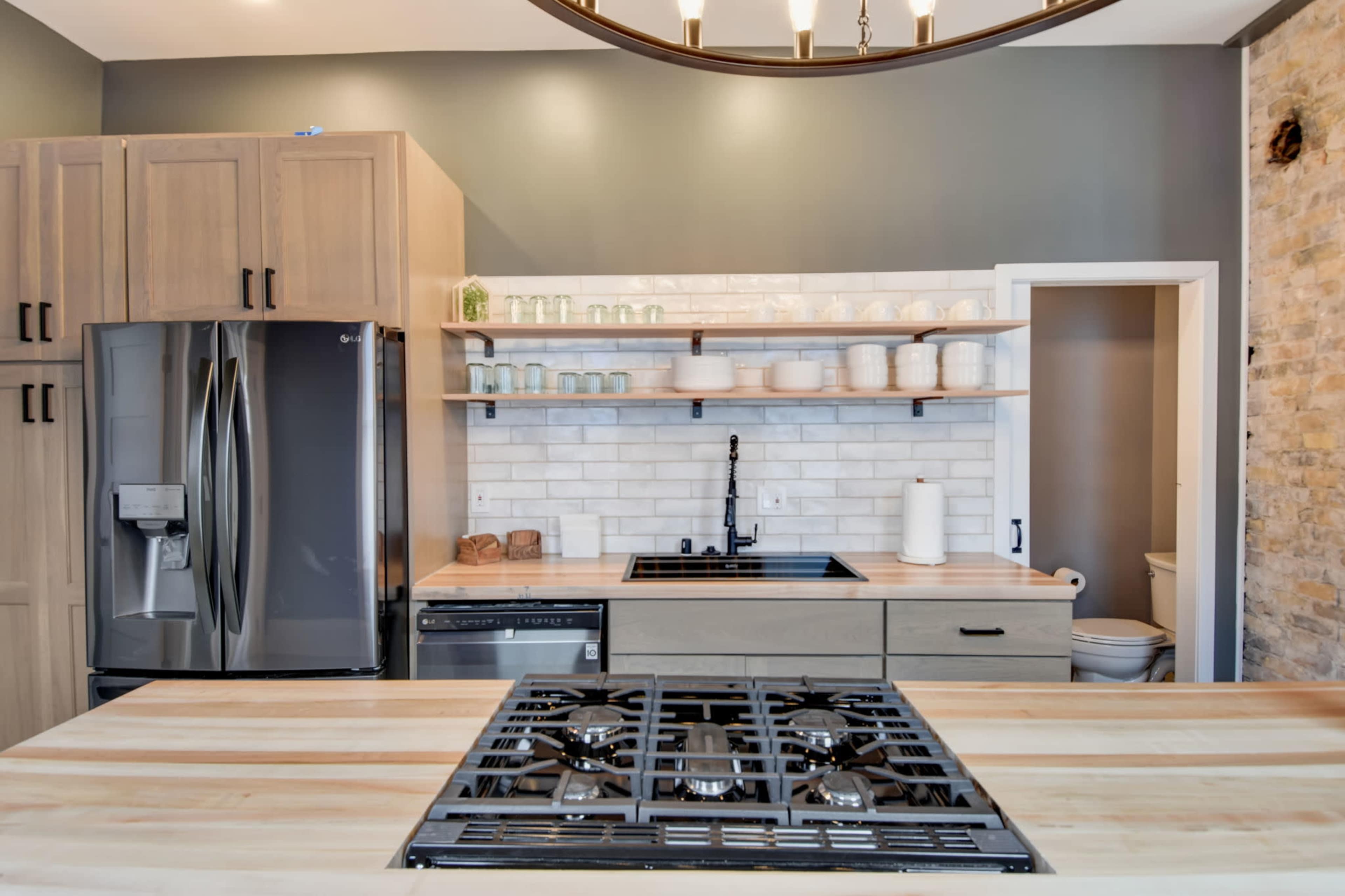 A modern kitchen with wooden cabinetry, a stainless steel refrigerator, and a gas cooktop featuring a black grill.