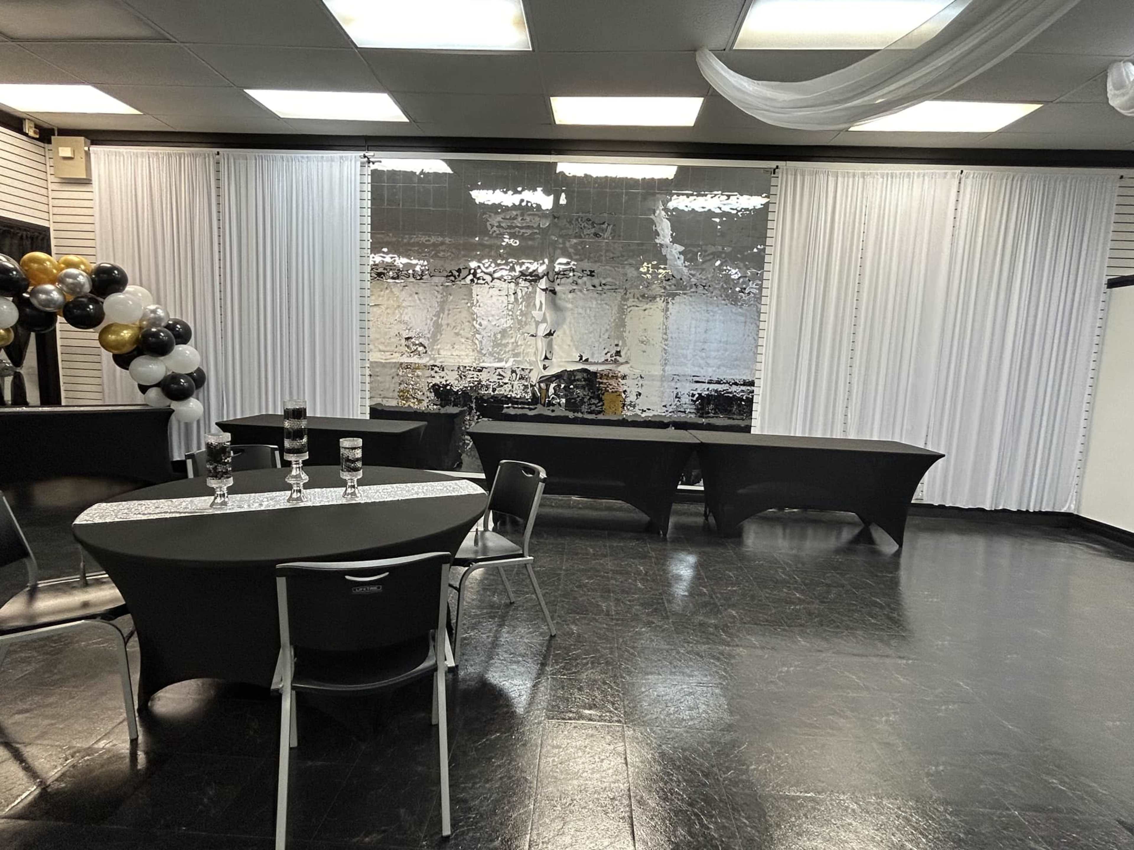 A banquet hall with black tablecloths, chairs, and draped white curtains, featuring a large mirrored backdrop.