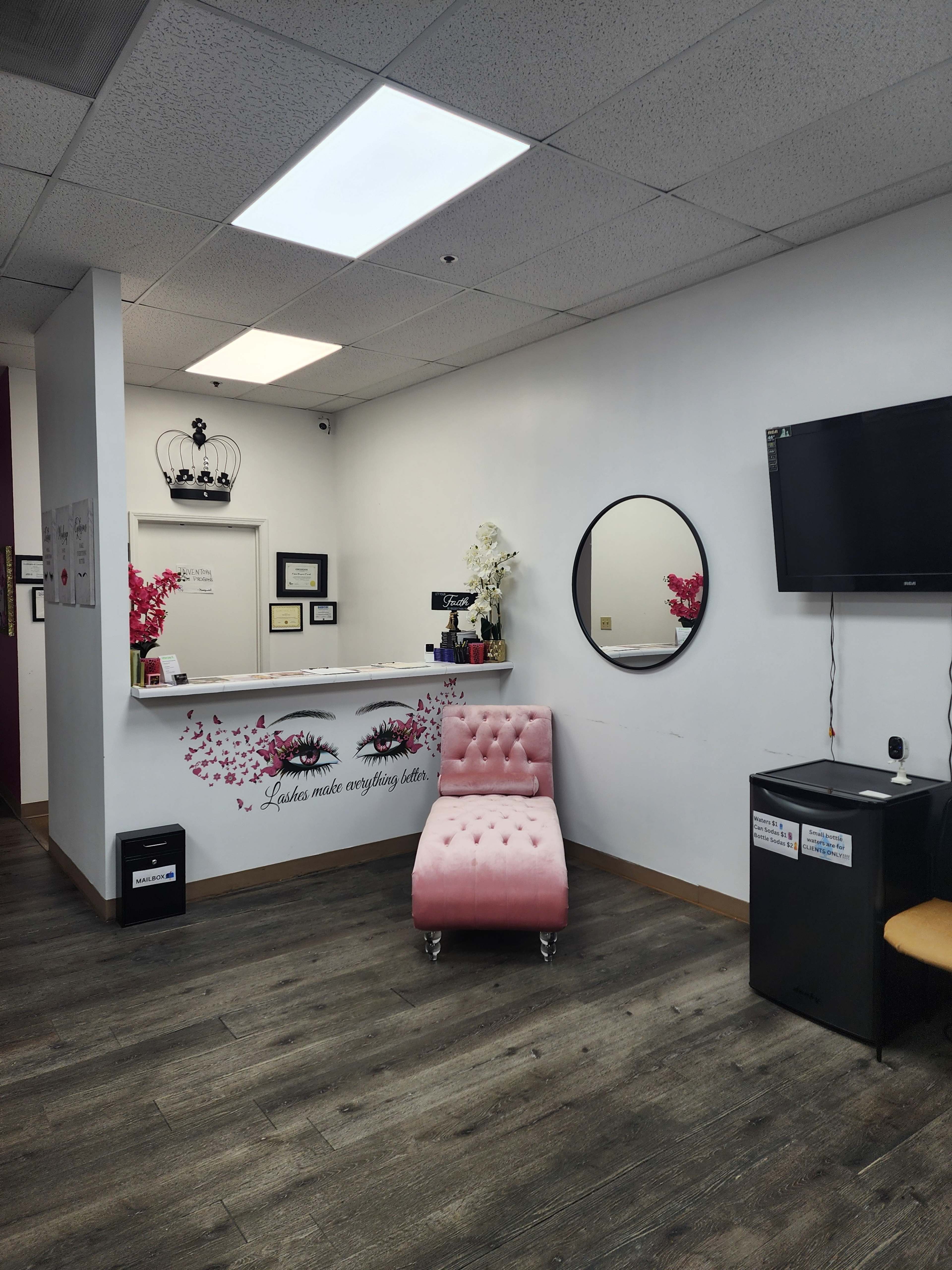 The image shows a beauty salon interior featuring a pink tufted chair, a circular mirror, a reception desk with decorative elements, and a television mounted on the wall.