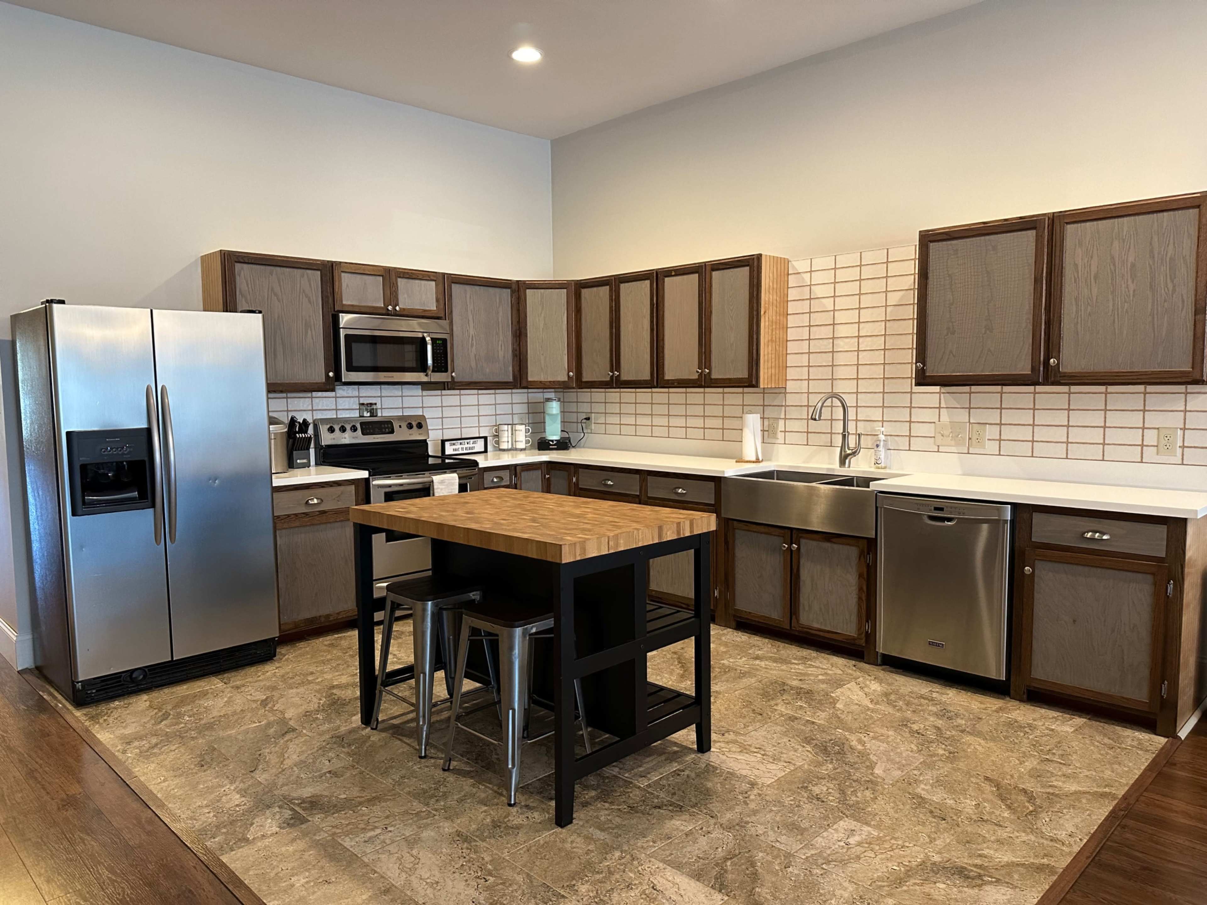 A modern kitchen featuring stainless steel appliances, wooden cabinetry, and a central island with stools.