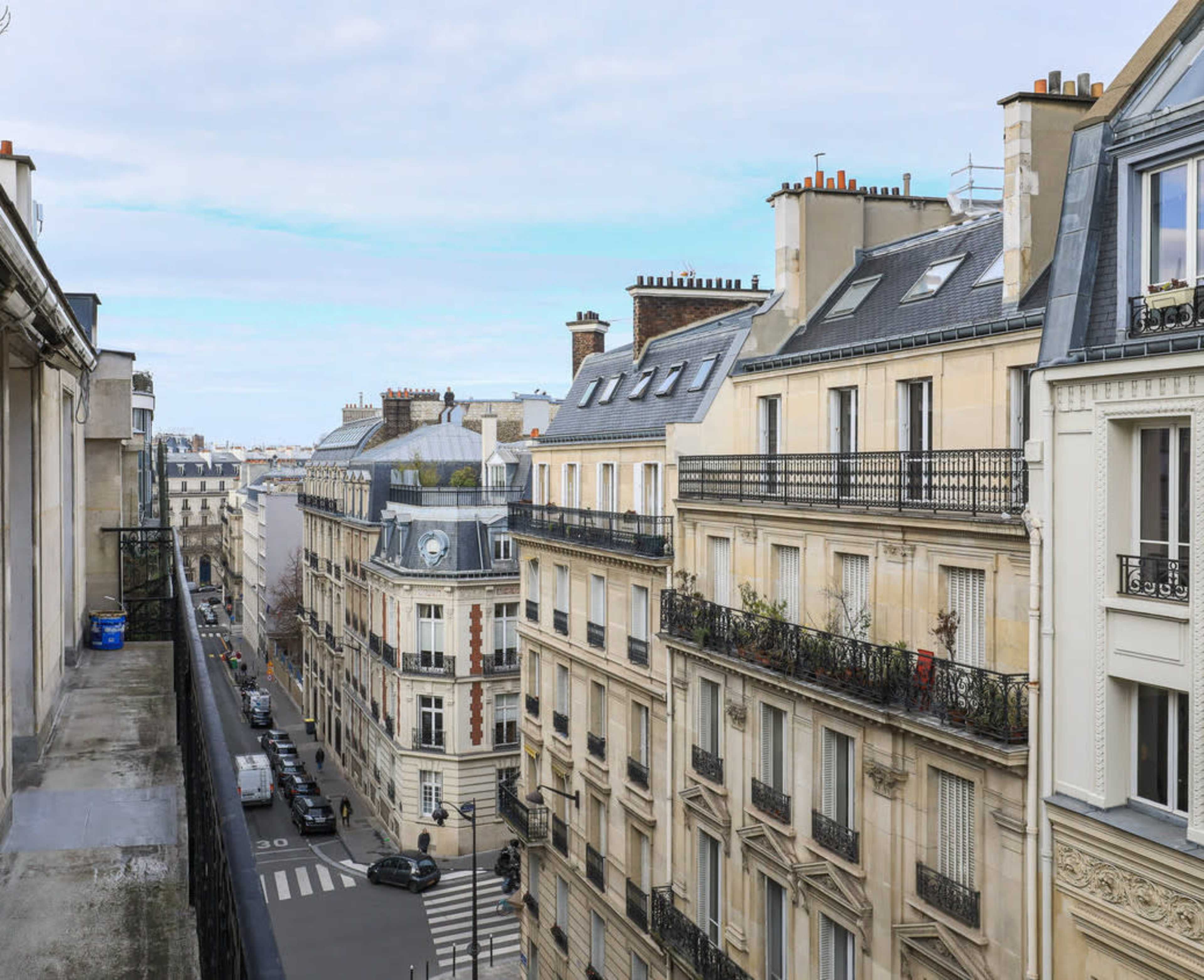 The image shows a city street in Paris lined with classic, five-story buildings and a clear sky overhead.