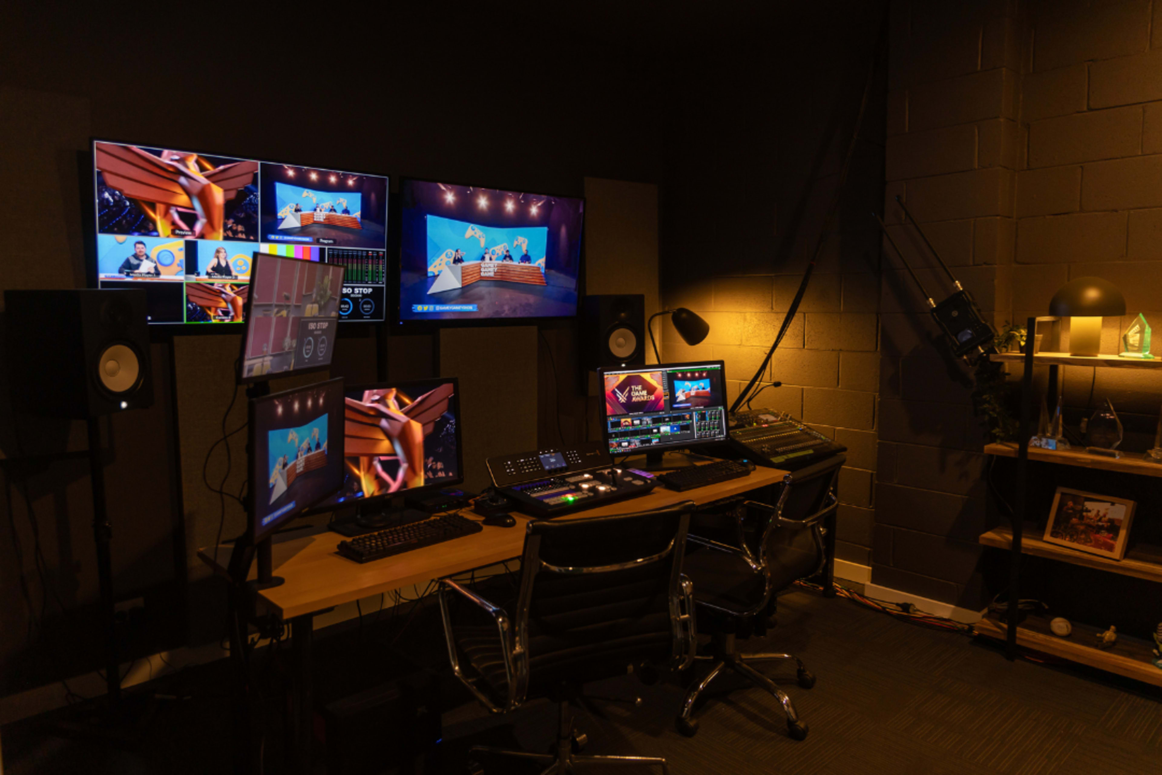 The image depicts a modern control room featuring multiple screens, video editing equipment, and a desk with professional audio-visual control devices.