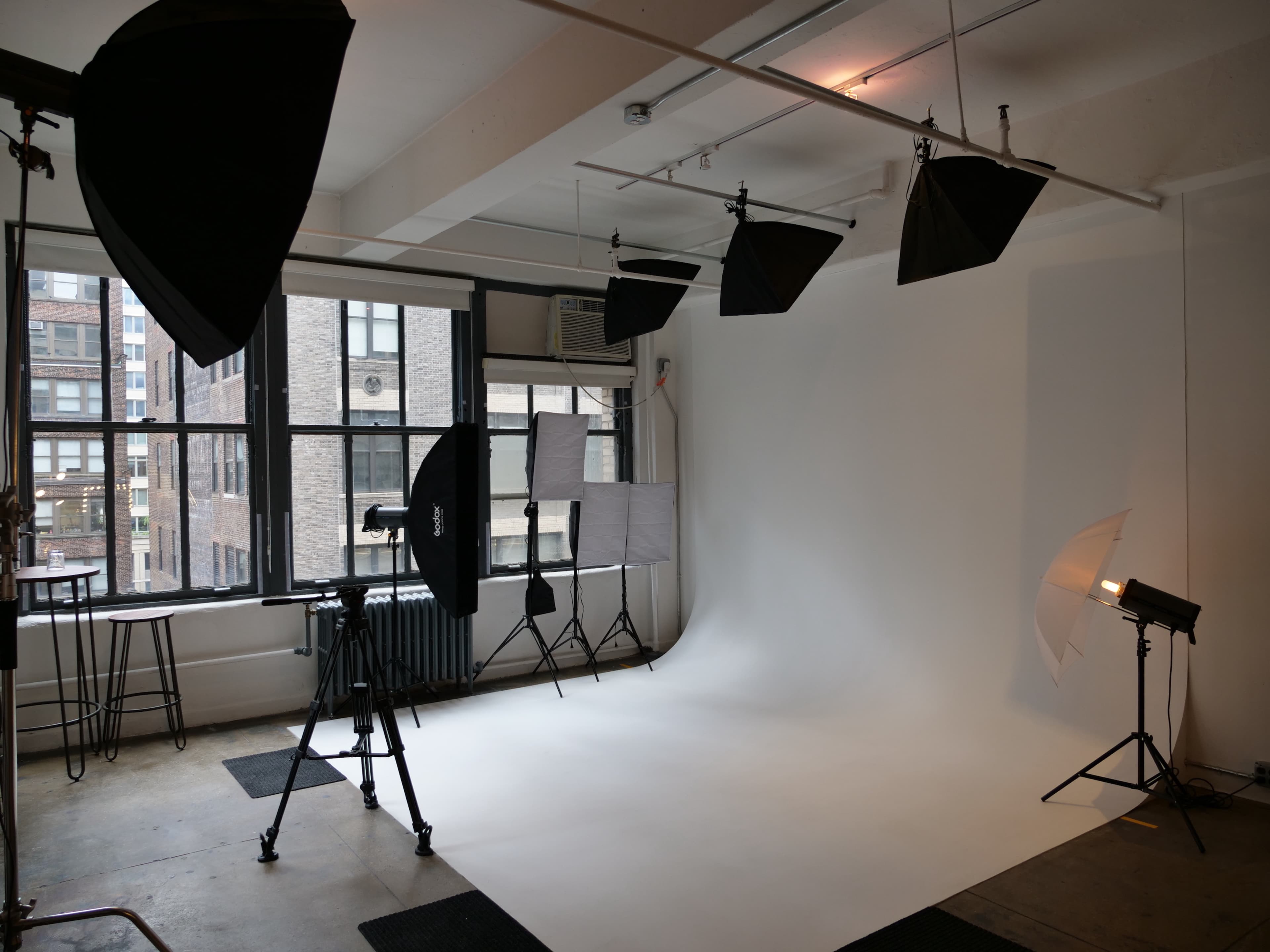 A photography studio with a seamless white backdrop, multiple lighting setups, and a camera on a tripod.