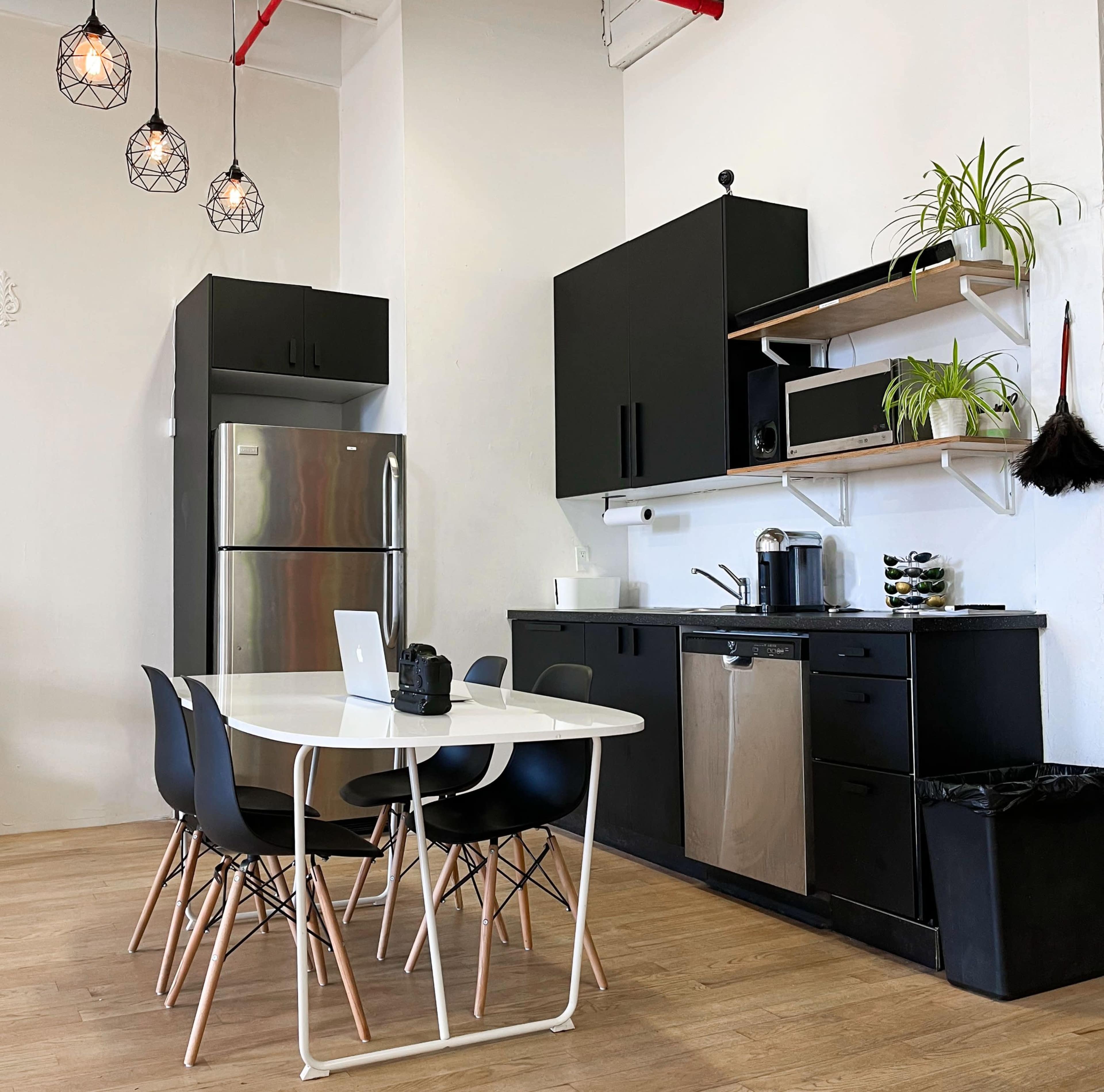 A modern kitchen with black cabinetry, stainless steel appliances, a white table with black chairs, and pendant lighting.