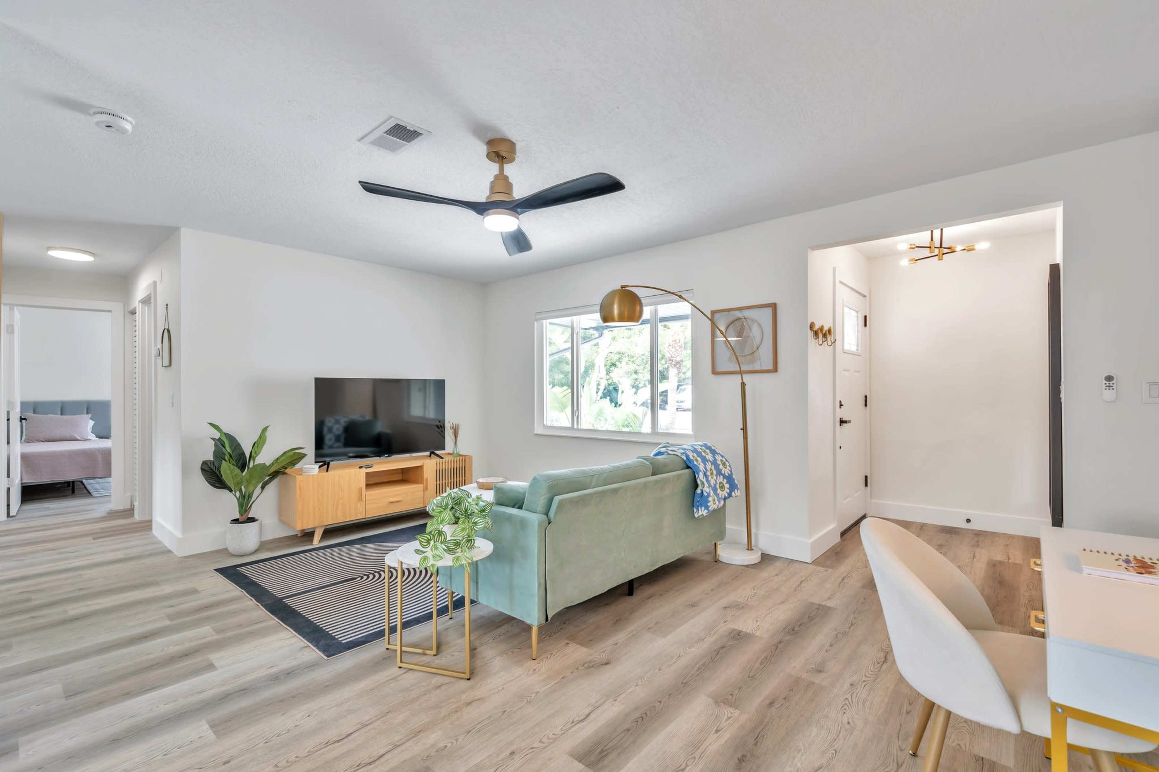 A modern living room with a light green sofa, a wooden TV stand, and large windows letting in natural light.